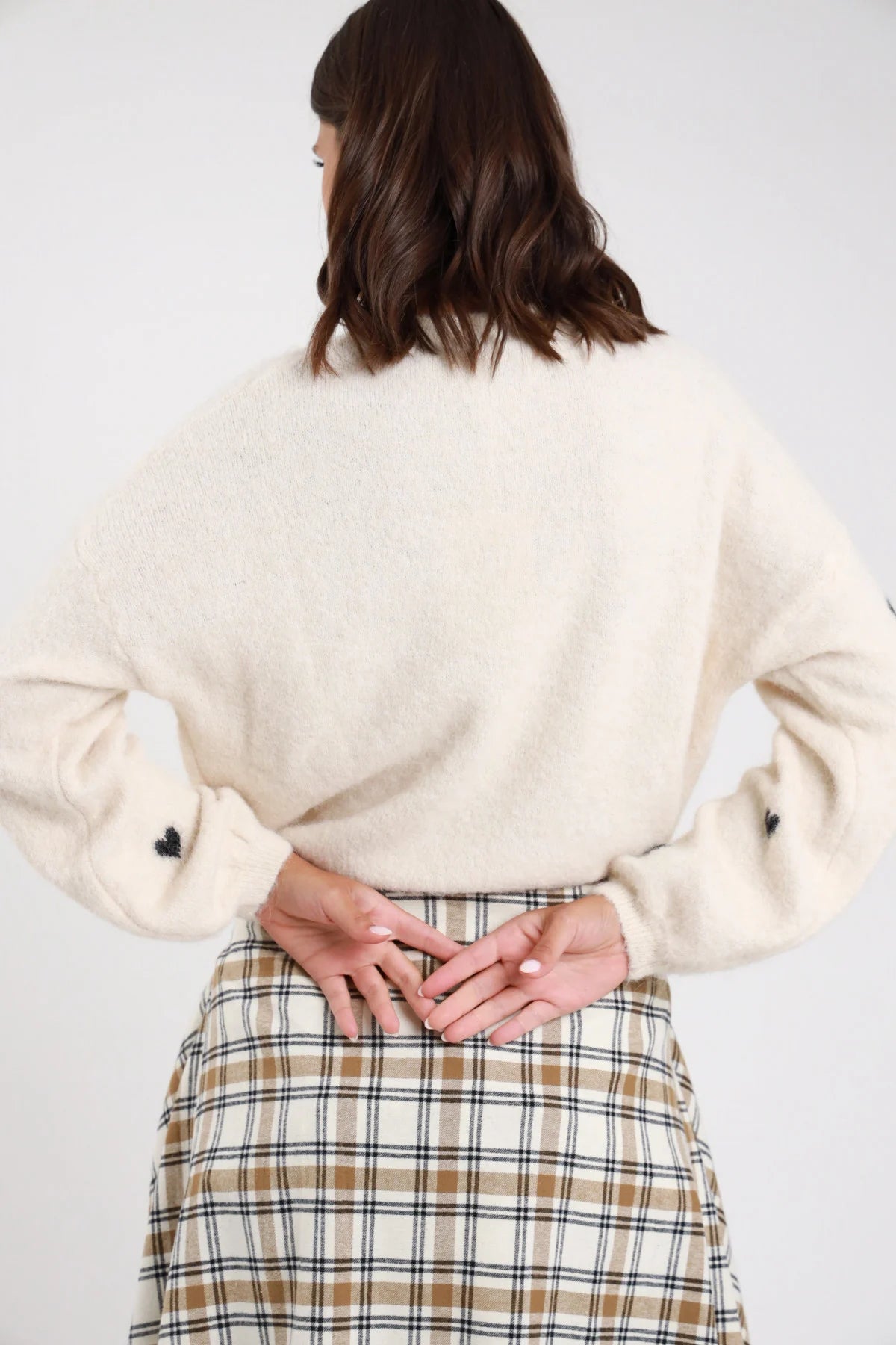 Pullover cuori jacquard tutto corpo eyelash bouclé balloon oversize girocollo costine avorio ecru cuori nero frontale busto braccia conserte mano sollevata - modella frontale busto braccia conserte mano destra sollevata sguardo frontale capelli castani scuri mossi sfondo bianco camicia check annodata vita jeans