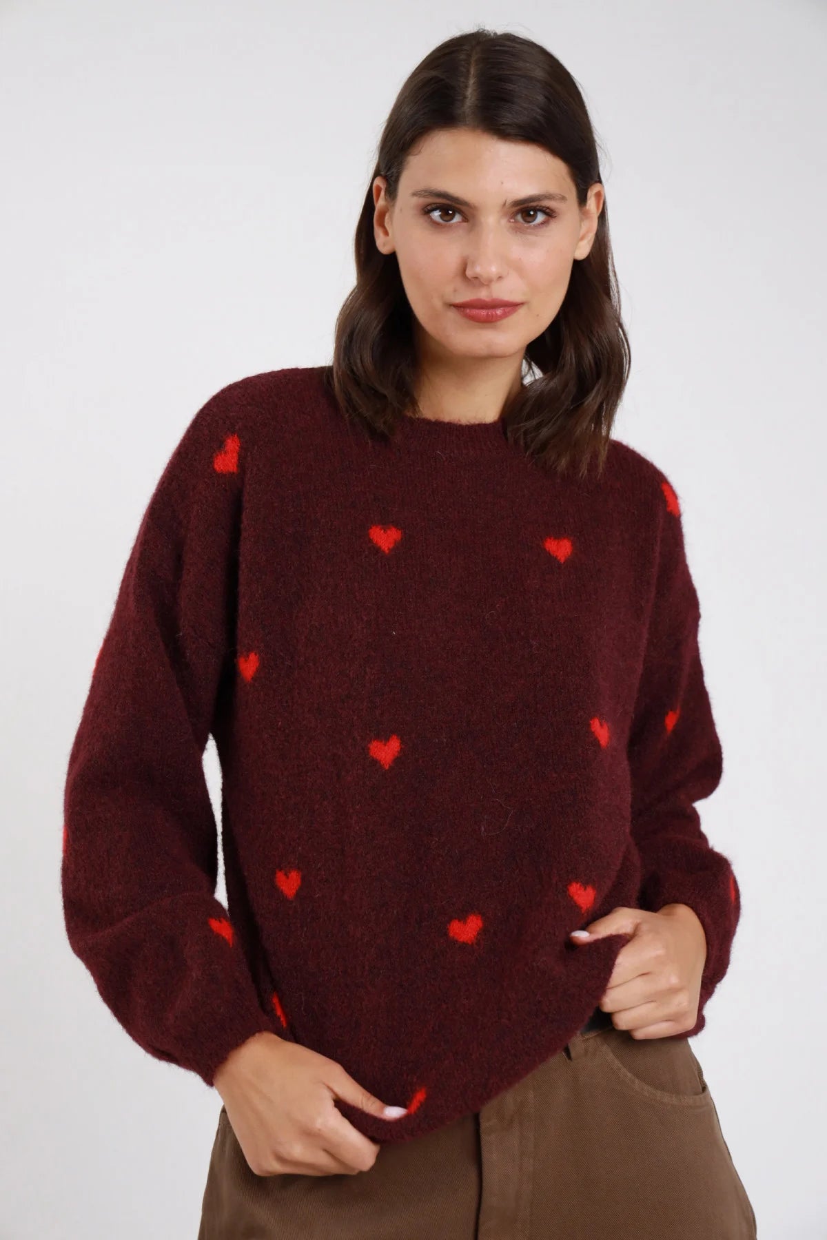 Pullover cuori jacquard tutto corpo eyelash bouclé balloon oversize girocollo costine bordeaux granata cuori rosso frontale busto mani fianchi - modella frontale busto mani fianchi sguardo frontale capelli castani scuri mossi sfondo bianco pantaloni marroni cammello