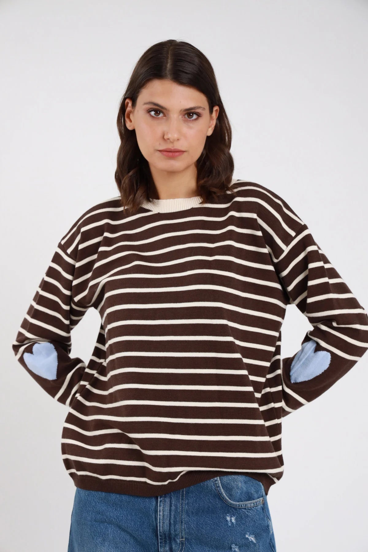 Pullover righe orizzontali bicolore cuori jacquard intarsiati gomiti marrone cioccolato avorio panna cuori azzurro baby blue frontale mani fianchi - modella frontale mani fianchi sguardo frontale capelli castani scuri ondulati sfondo bianco jeans blu chiaro strappato