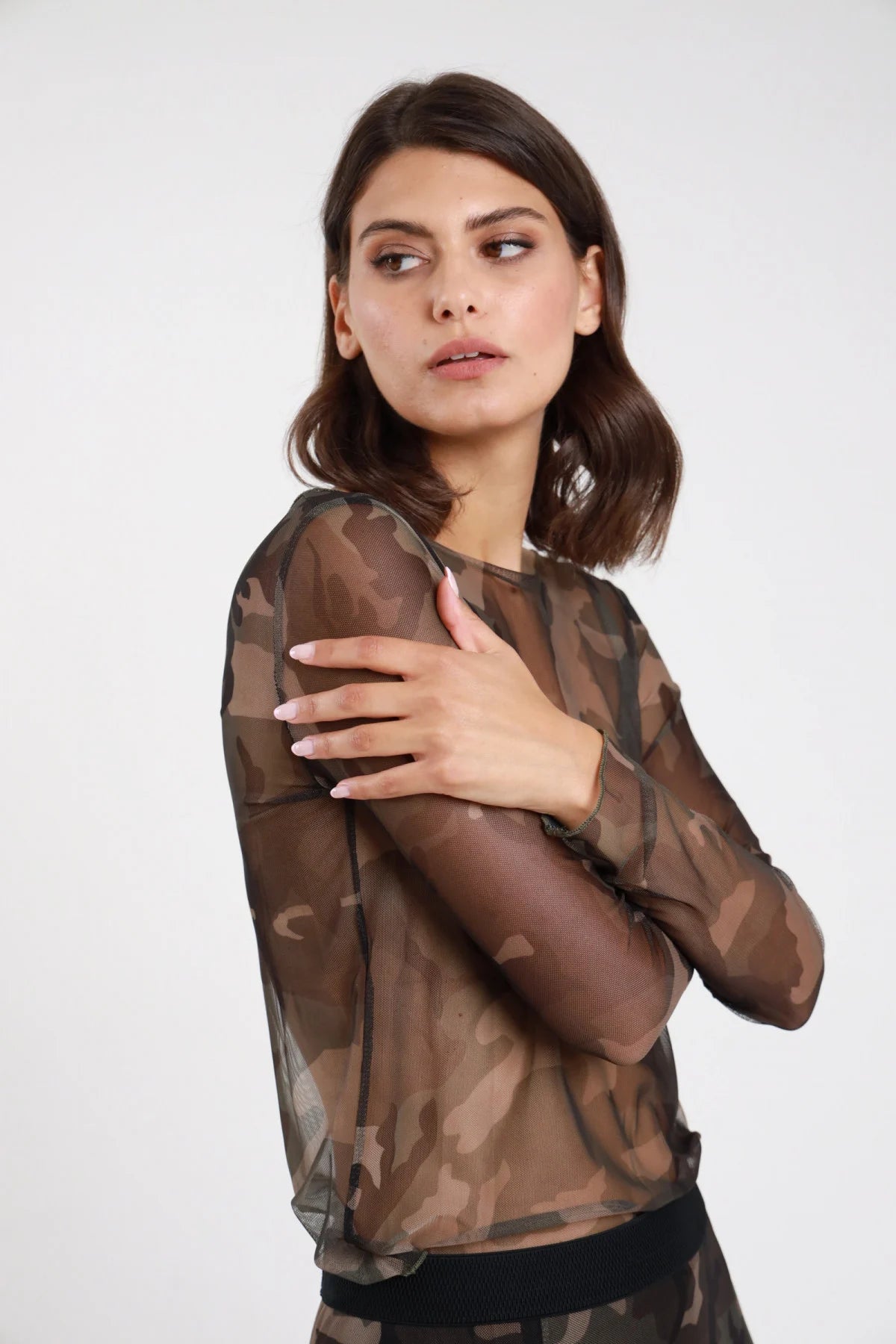 Maglia tulle mimetica militare donna semitrasparente scollo barca maniche lunghe second-skin - vista laterale tre quarti mano sul petto con gonna midi mimetica