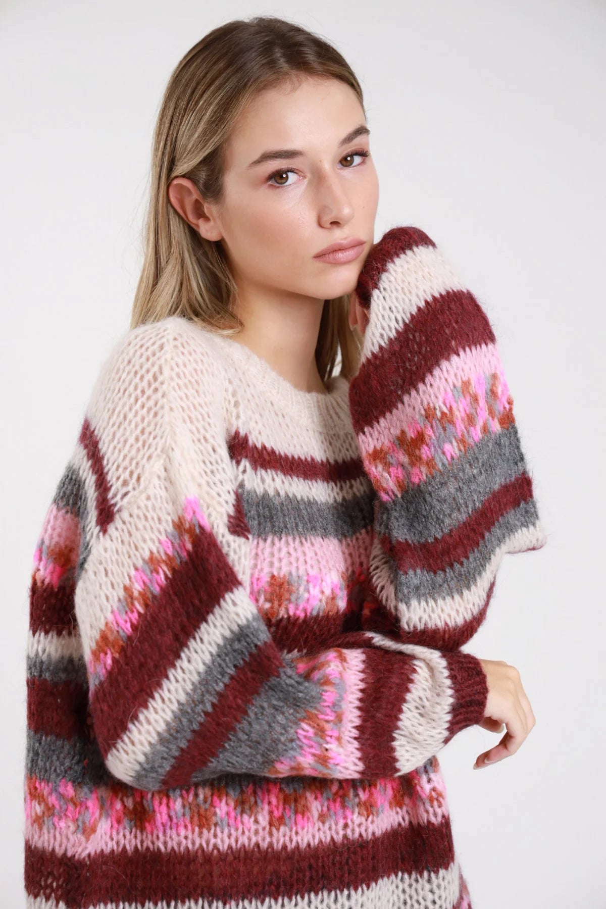 Maglione mohair righe panna bordeaux grigio rosa fluo jacquard floreale - modella busto frontale ravvicinato mano al viso sguardo laterale pantaloni grigi capelli biondi lisci