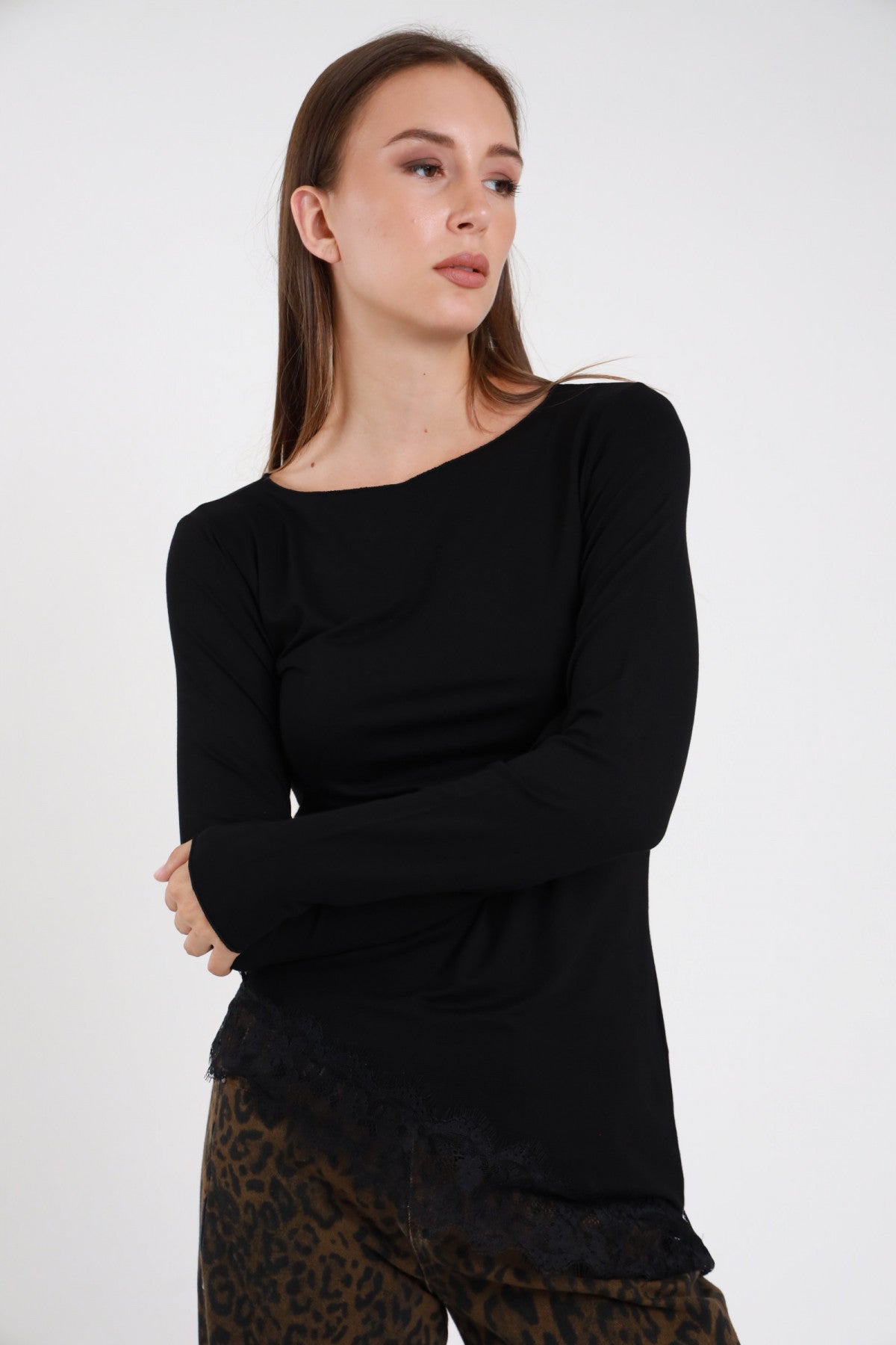 Maglia pizzo asimmetrica nera donna collo barchetta maniche lunghe aderente fondo asimmetrico - vista tre quarti braccia conserte con pantaloni leopardati marroni