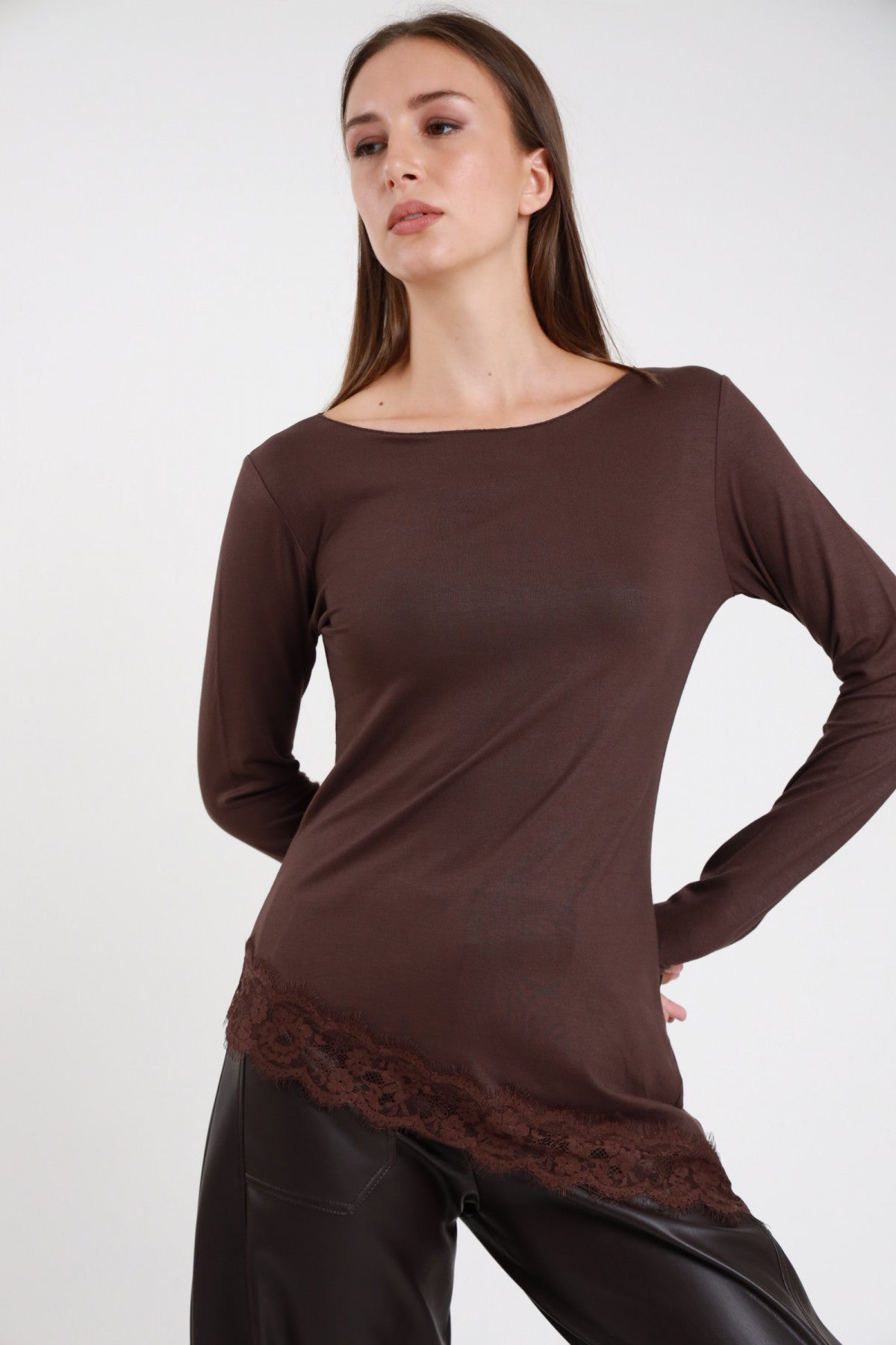 Maglia pizzo asimmetrica marrone cioccolato donna collo barchetta maniche lunghe bordo pizzo floreale tono su tono - vista frontale mano sul fianco con pantaloni in ecopelle neri