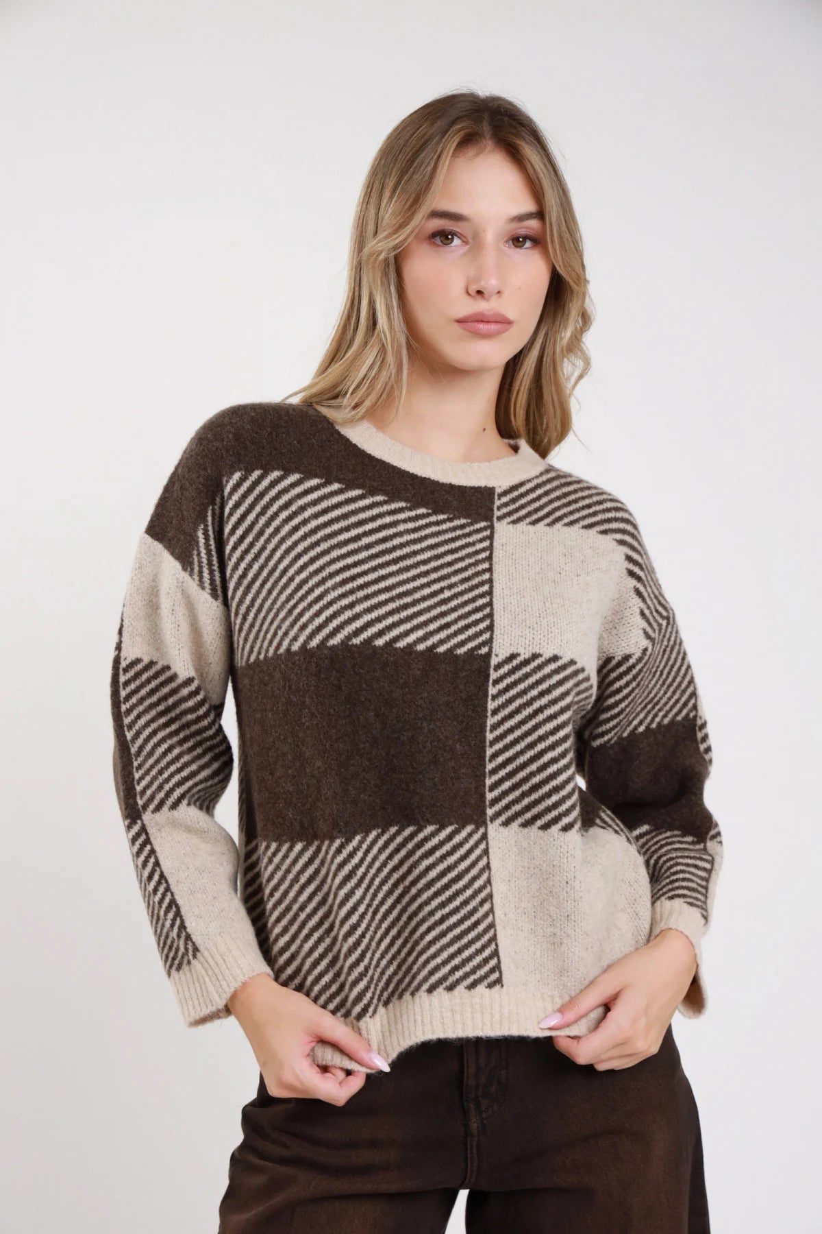 Pullover quadri patchwork cioccolato sabbia caramello frontale busto mani incrociate jacquard maxi quadri bicolor righe diagonali girocollo costina dropped shoulder - modella frontale busto mani incrociate grembo sguardo frontale jeans cioccolato capelli biondi mossi