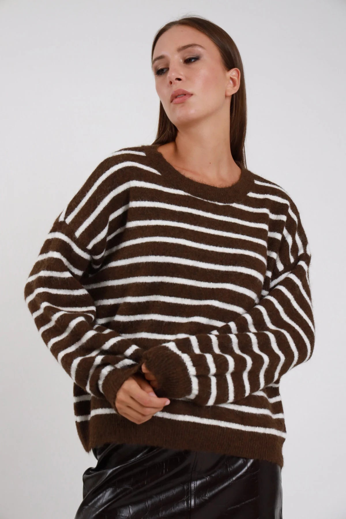 Pullover Girocollo Oversize Righe Orizzontali marrone cioccolato bianco panna misto lana effetto alpaca manica raglan ampia polsino costina silhouette boxy - modella busto frontale posa mani incrociate davanti sguardo basso soft capelli castani lisci sfondo bianco gonna ecopelle nera lucida