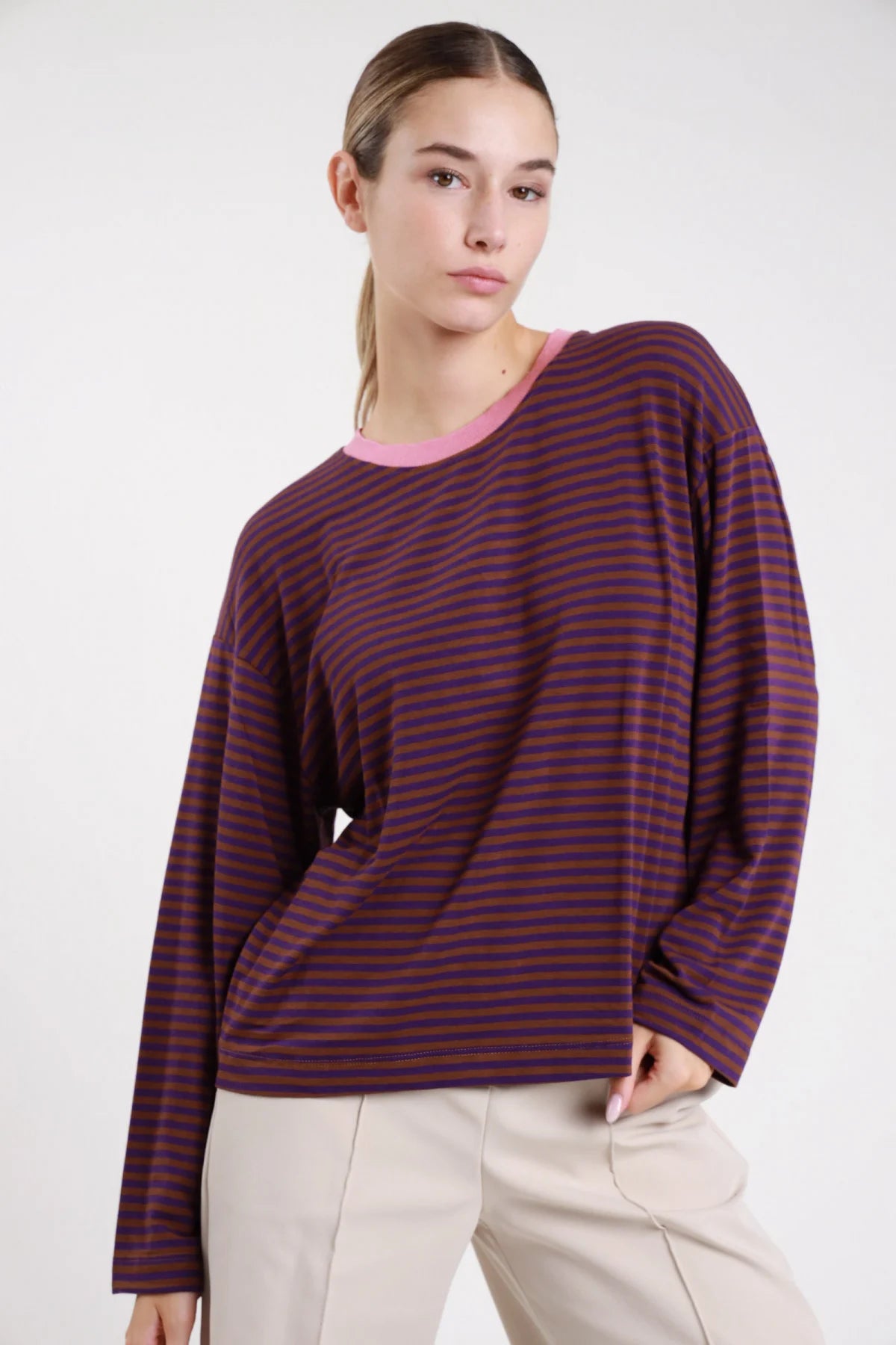 Maglia righe bicolor prugna viola frontale busto mano fianco girocollo costina rosa cipria manica lunga dropped shoulder boxy - modella frontale busto mano fianco sguardo frontale pantaloni beige capelli castani raccolti