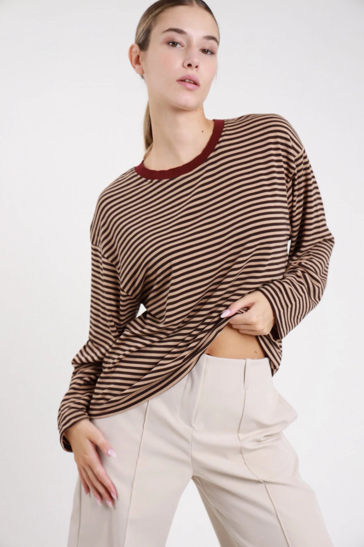 Maglia righe bicolor cammello cioccolato frontale busto braccia conserte girocollo costina borgogna manica lunga oversize - modella frontale busto braccia conserte sguardo frontale pantaloni beige capelli castani raccolti