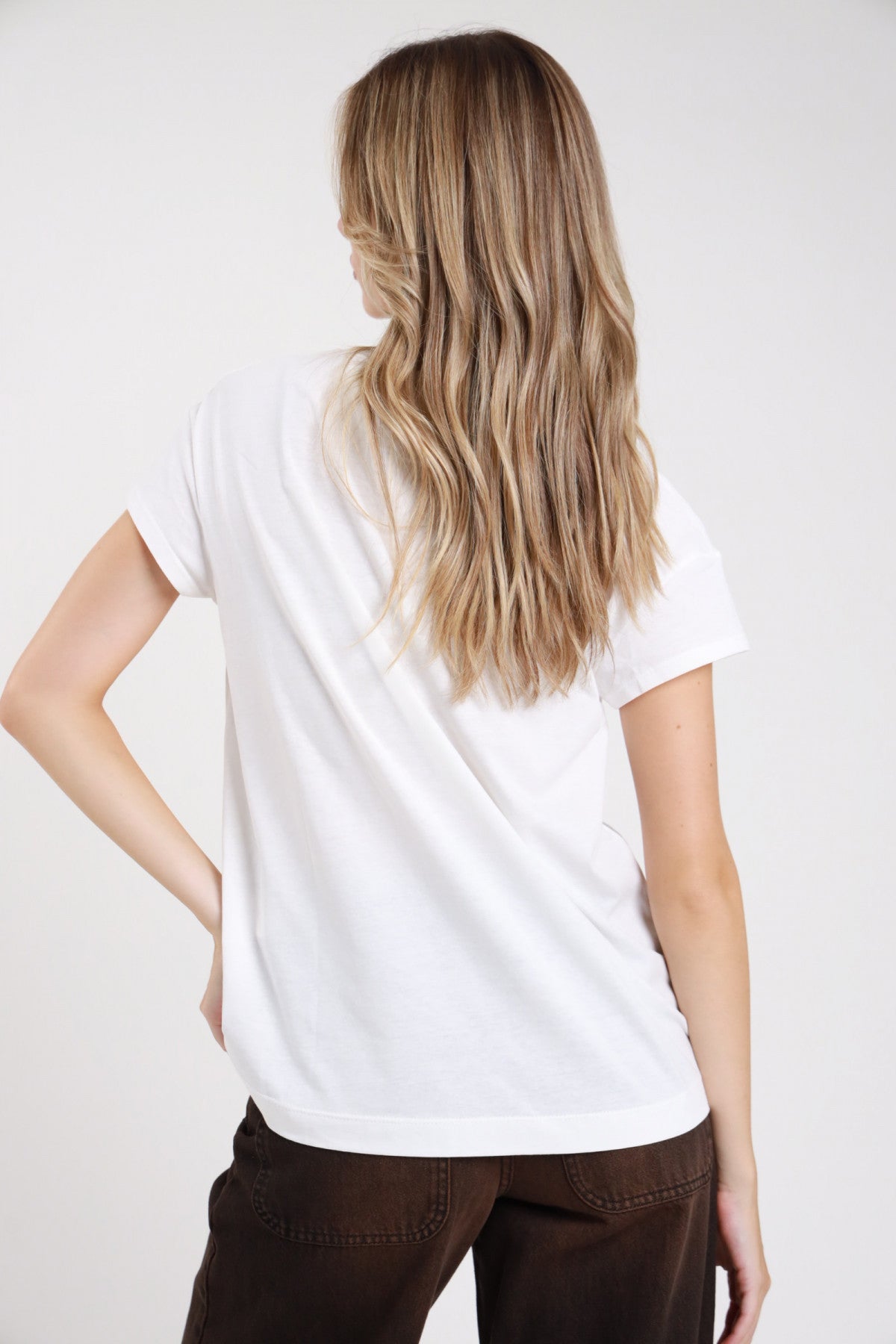 T-shirt rock tour grafica bianca retro intera manica corta cuff risvolto corpo boxy oversize orlo dritto - modella retro intera mano fianco sguardo posteriore pantaloni marrone scuro capelli biondi ondulati lunghi