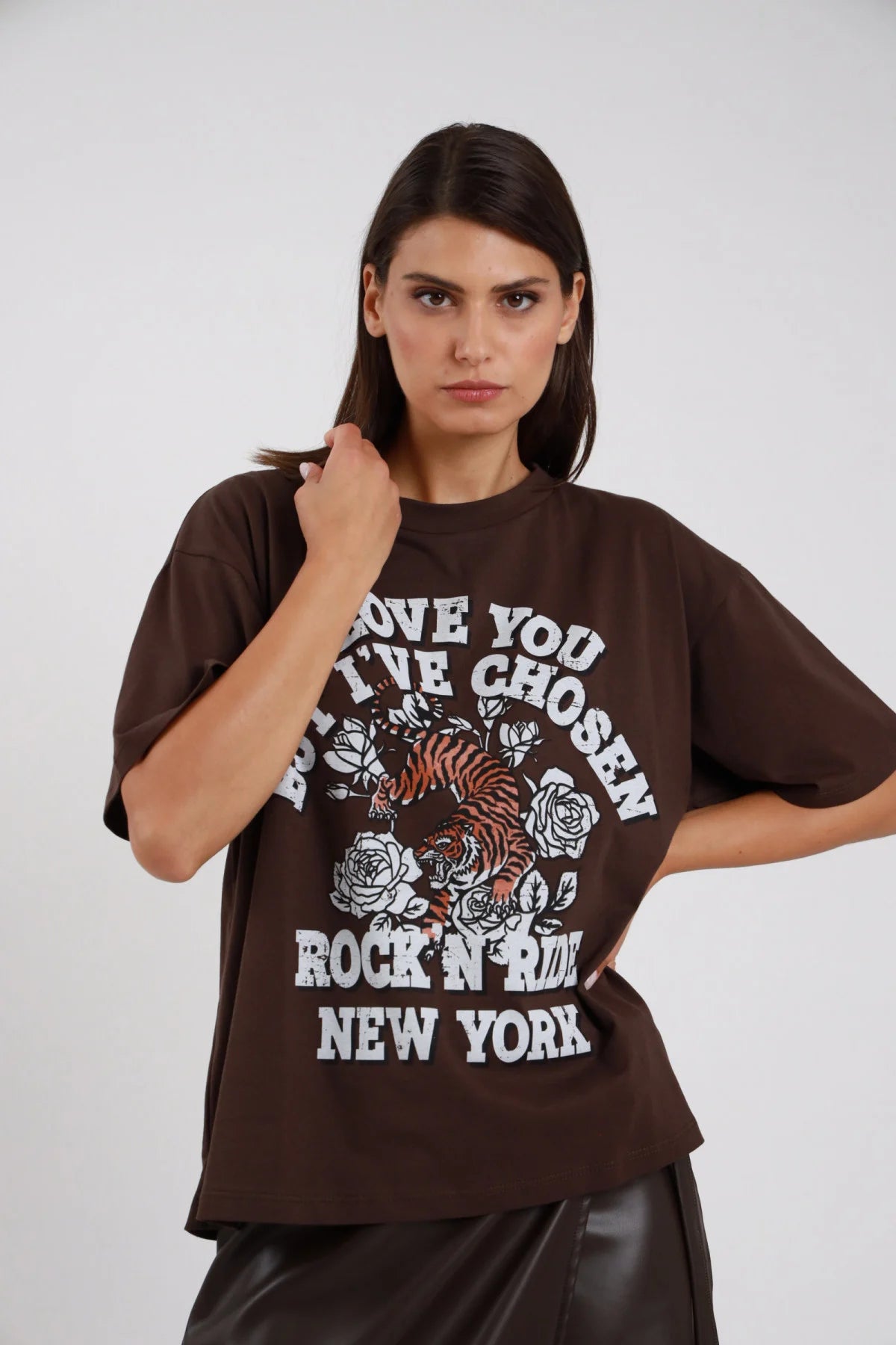 T-shirt Stampa rock tiger marrone cioccolato scuro oversize drop shoulder crop boxy stampa bianca tigre rose tattoo Rock'N Ride New York busto frontale 3/4 mano collo sguardo diretto - modella busto frontale 3/4 mano collo sguardo camera capelli castani lisci sfondo bianco gonna ecopelle nera