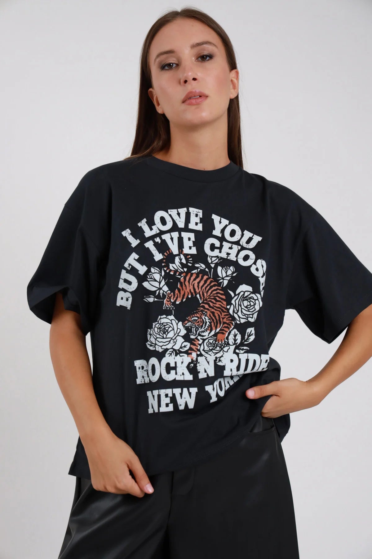 T-shirt Stampa rock tiger nero antracite scuro oversize drop shoulder crop boxy stampa bianca tigre rose tattoo Rock'N Ride New York busto frontale 3/4 mano fianchi sguardo camera - modella busto frontale 3/4 mano fianchi sguardo camera capelli castani lisci sfondo bianco pantaloni neri ecopelle