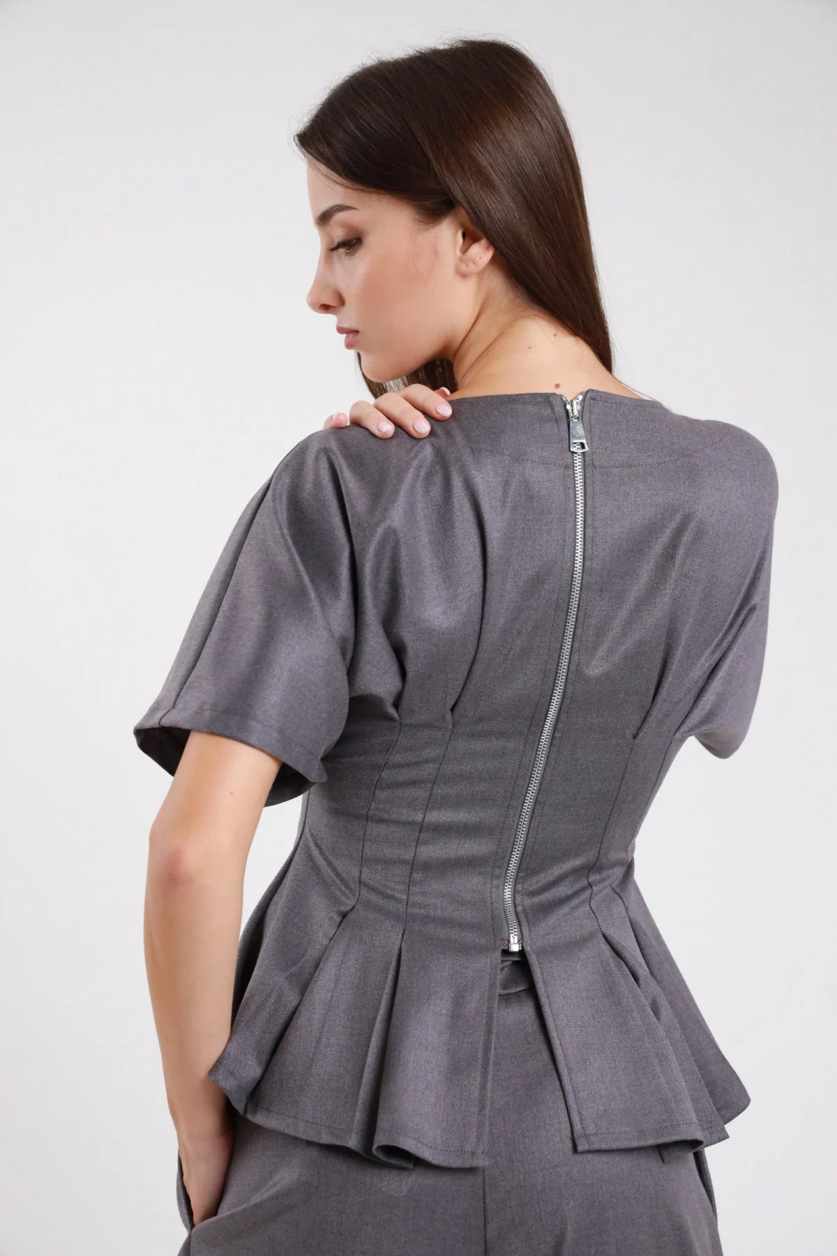 Top maglia sartoriale grigio ardesia antracite crêpe stretch retro zip centrale posteriore argento metallica corset pince verticali manica corta flutter campana peplum doppio balze sfalsate - modella retro intera mano spalla sguardo basso laterale capelli castani scuri lisci sfondo bianco gonna check grigio a strati abbinata coordinata