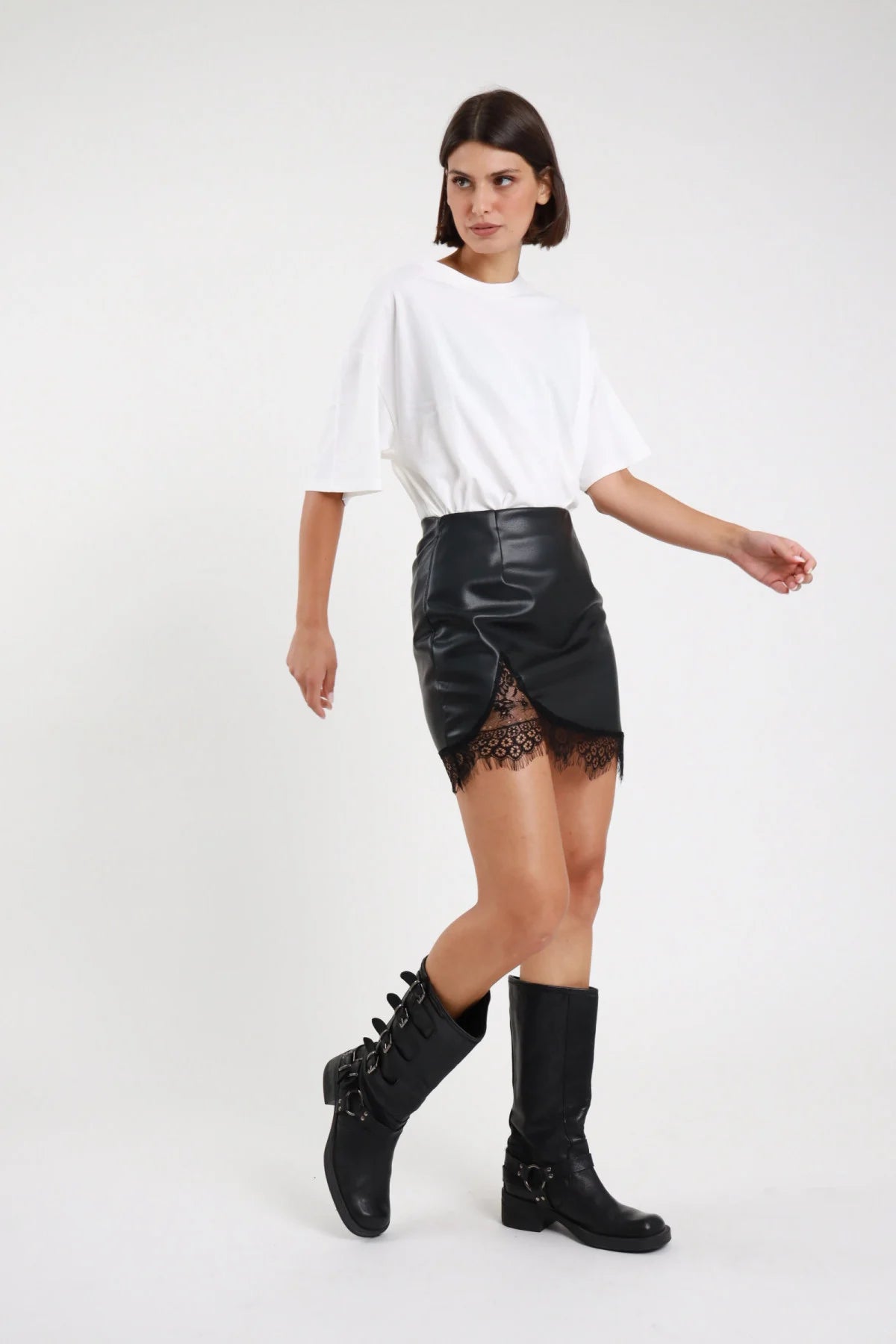 Minigonna ecopelle pizzo Susy Mix nera con orlo incrociato, indossata con T-shirt bianca e stivali neri