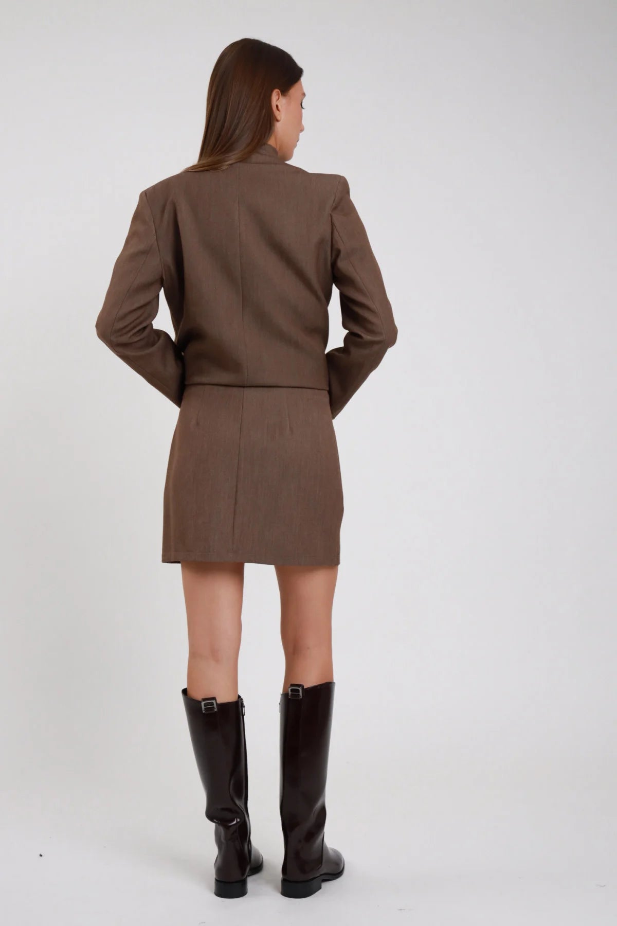 Minigonna sartoriale marrone cioccolato vita alta mini dritta tubino stretch retro intera schiena coordinata blazer mantella marrone - modella retro intera capelli castani lisci sfondo bianco blazer mantella marrone stivali neri alti ginocchio tacco basso