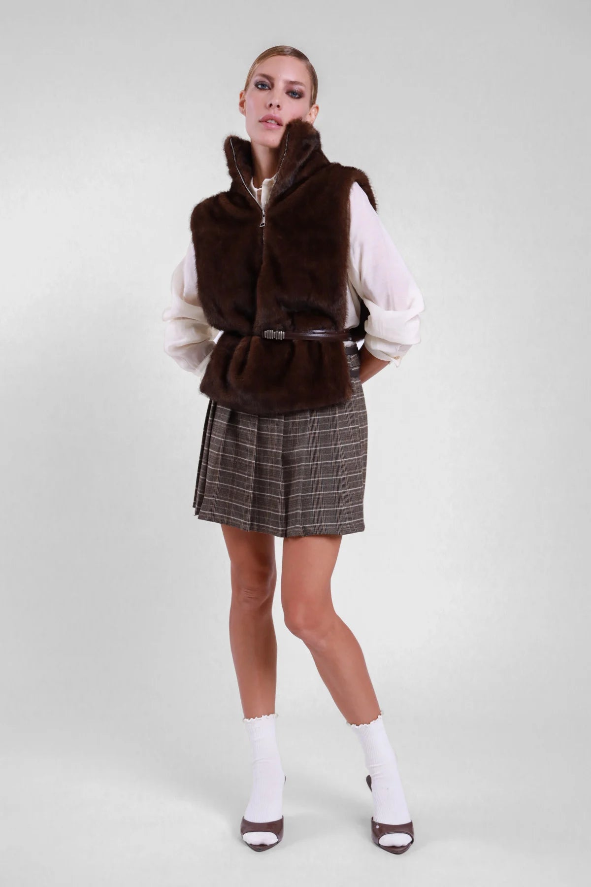 Minigonna pieghe check Susy Mix, vista frontale a figura intera con camicia chiara e gilet in ecopelliccia