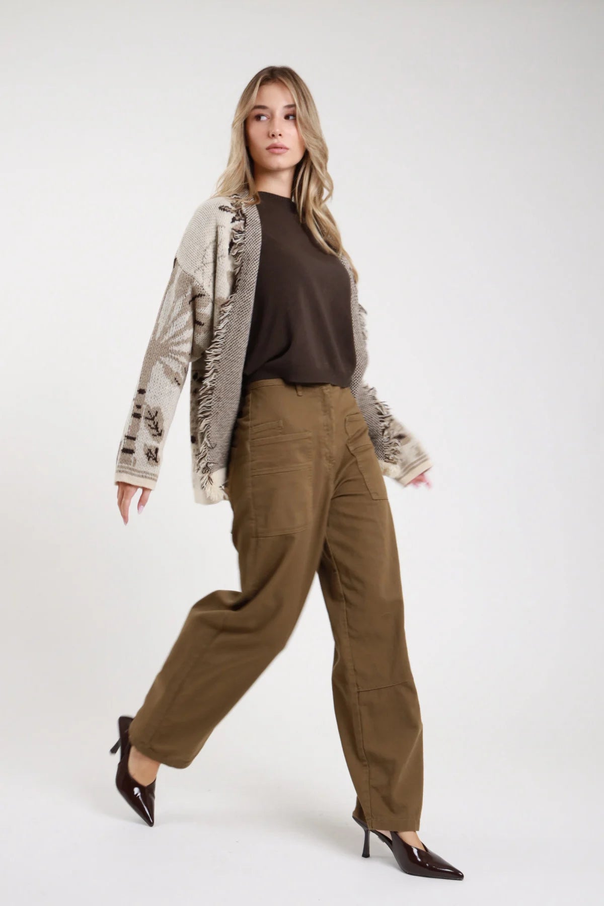 Jeans Tinto Capo Tasconi verde oliva khaki wide barrel tasconi applicati vita alta frontale intera posa camminata - modella frontale intera posa camminata sguardo laterale capelli biondi ondulati sfondo bianco cardigan fantasia beige t-shirt marrone décolleté nere