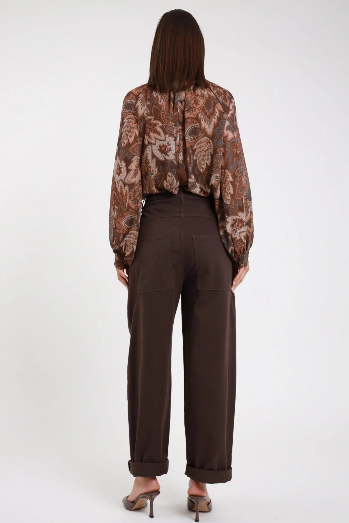 Jeans Tinto Capo Tasconi marrone cioccolato scuro wide barrel tasche posteriori vita alta risvolto retro intera schiena - modella retro intera capelli castani lisci sfondo bianco blusa paisley marrone sandali marroni tacco