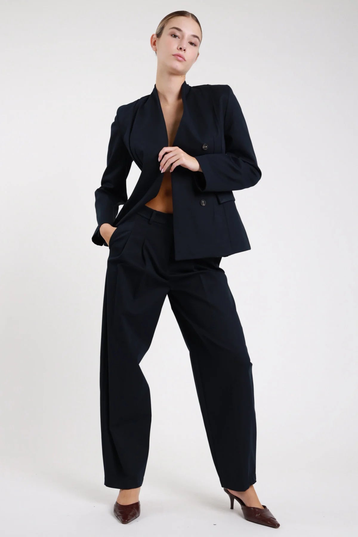 Pantaloni doppia pinces nero vita alta tailleur - modella frontale intera con blazer abbinato mano sul petto décolleté marroni capelli raccolti
