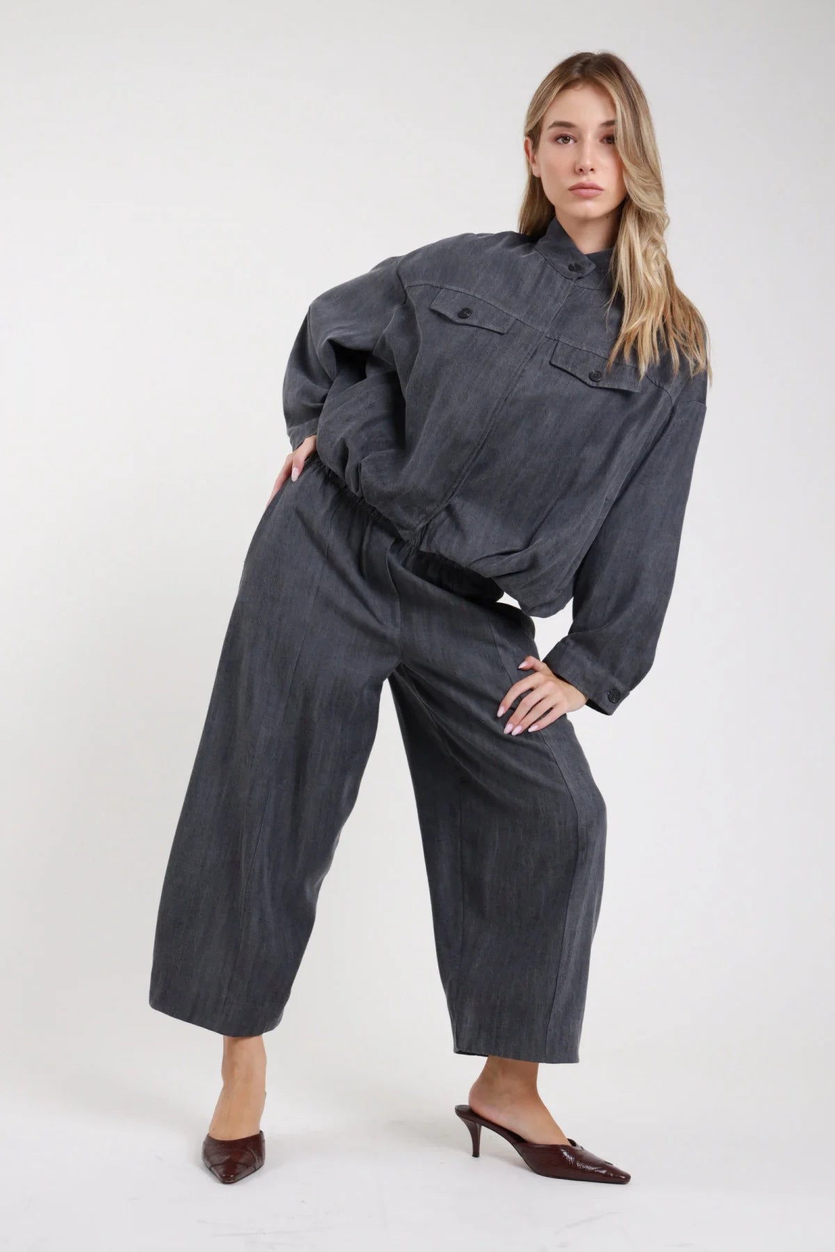 Pantalone gamba larga balloon lino antracite grigio scuro morbido - modella frontale intera mani sui fianchi con bomber abbinato antracite mules bordeaux capelli biondi mossi