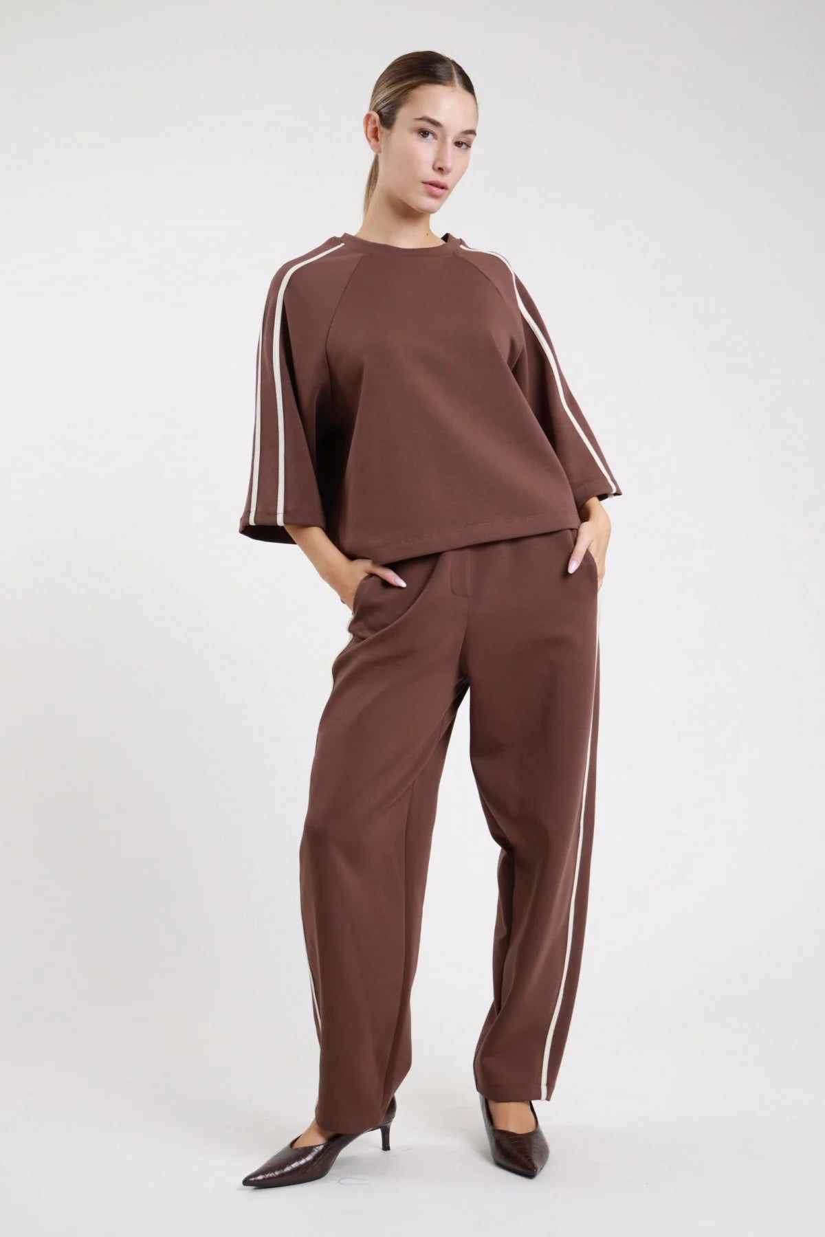 Pantalone barrel bande verde oliva laterale tre quarti coordinato felpa oliva bande nere gamba barrel carrot bande verticali nere - modella laterale tre quarti mani vita sguardo laterale felpa oliva bande nere sneaker nere capelli castani raccolti