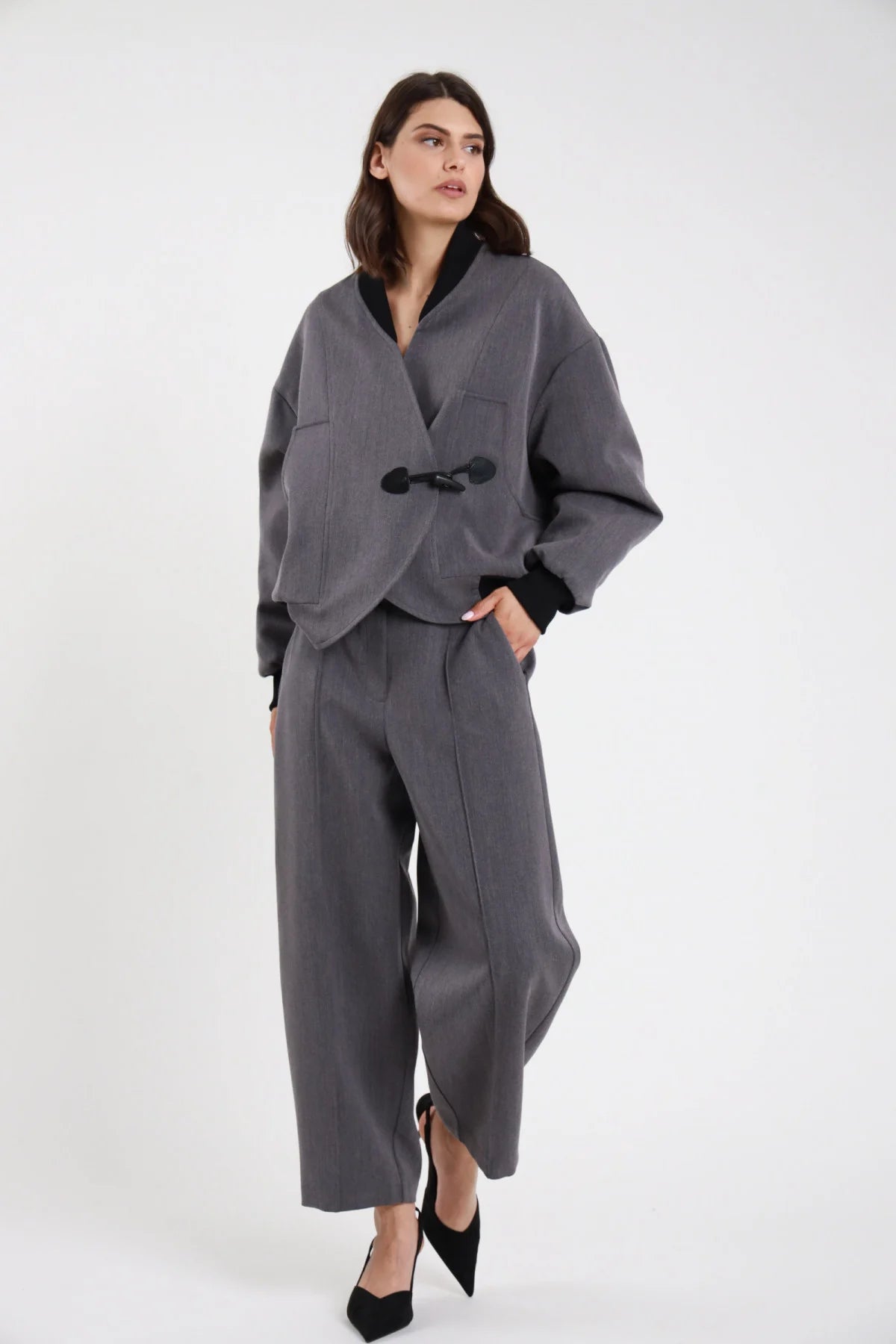 Pantalone Ovetto barrel grigio melange vita alta pinces tasche filetto gamba balloon scultorea cropped 7/8 frontale intera con Bomber Alamaro grigio melange alamaro nero - modella frontale intera sguardo laterale capelli castani scuri sfondo bianco bomber grigio melange slingback neri tacco