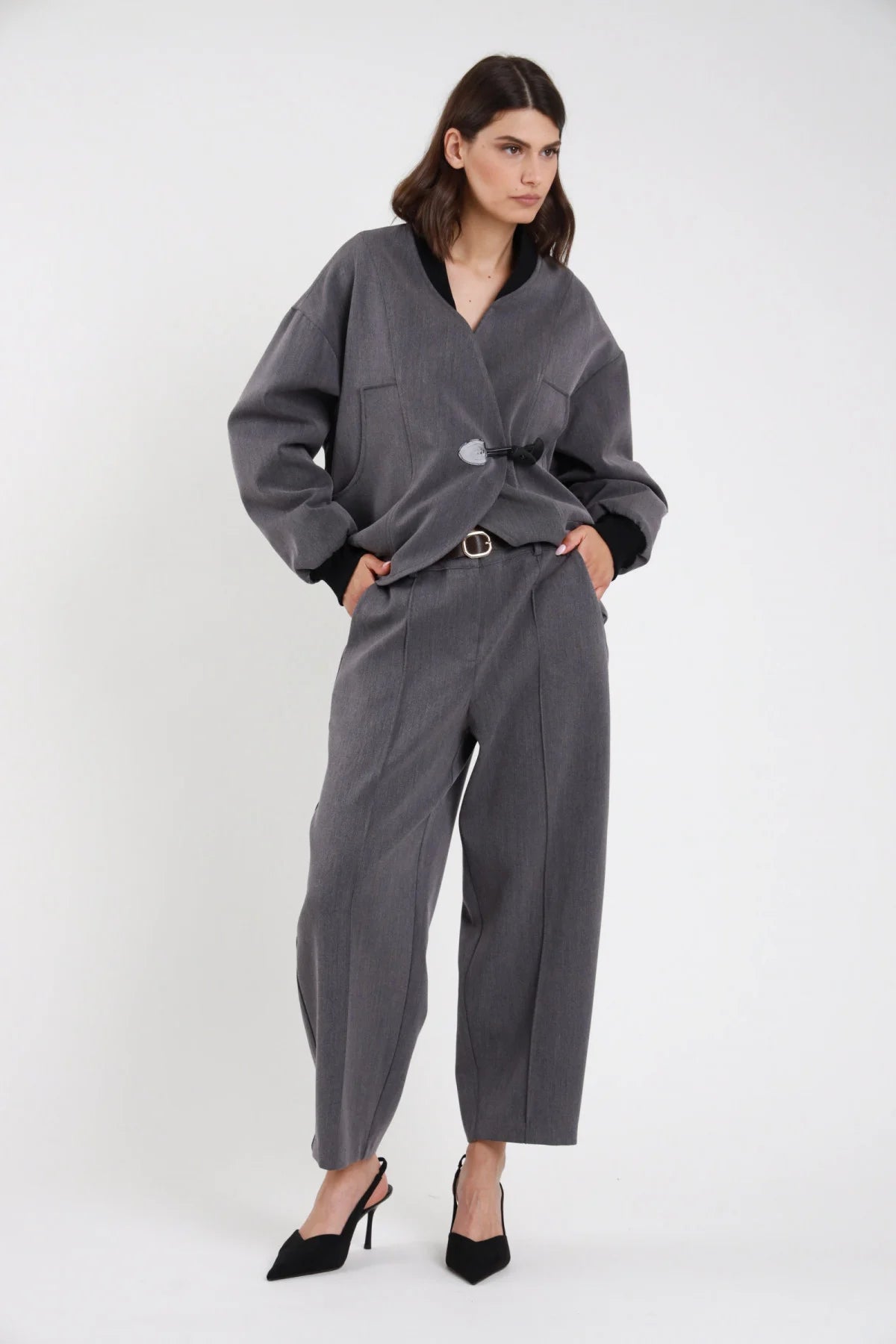 Pantalone Ovetto barrel grigio melange vita alta pinces tasche filetto gamba balloon scultorea cropped 7/8 frontale intera mani tasche con Bomber Alamaro e cintura thin dorata - modella frontale intera mani tasche sguardo frontale capelli castani scuri sfondo bianco bomber grigio alamaro nero cintura thin dorata slingback neri