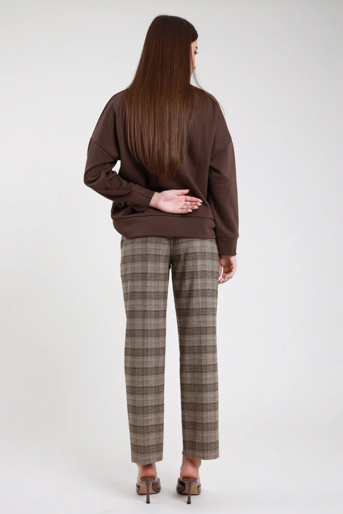 Pantaloni check principe di Galles sartoriali beige marrone nero gamba dritta straight piega centrale vita media caviglia retro intera mano schiena capelli lunghi - modella retro intera mano schiena sguardo giù capelli castani lisci lunghi sfondo bianco mules tacco marroni felpa marrone
