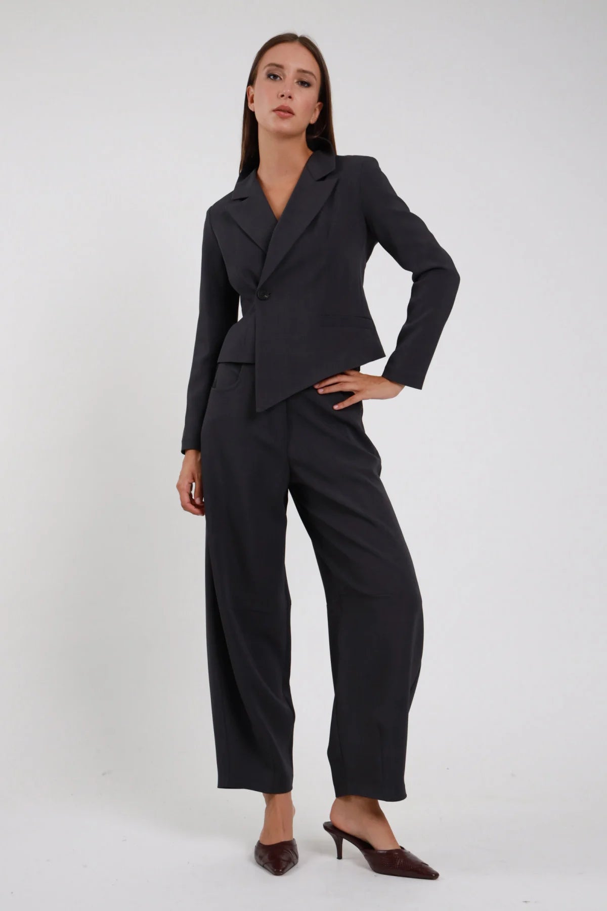 Pantalone Ovetto grigio antracite nero carbone vita alta passanti cintura forma barrel scultorea pancia ampia orlo stretto caviglia silhouette strutturata frontale intera posa statica mano fianco sguardo frontale - modella frontale intera posa statica mano fianco sguardo frontale capelli castani sfondo bianco blazer asimmetrico grigio coordinato sabot marrone croco tacco kitten