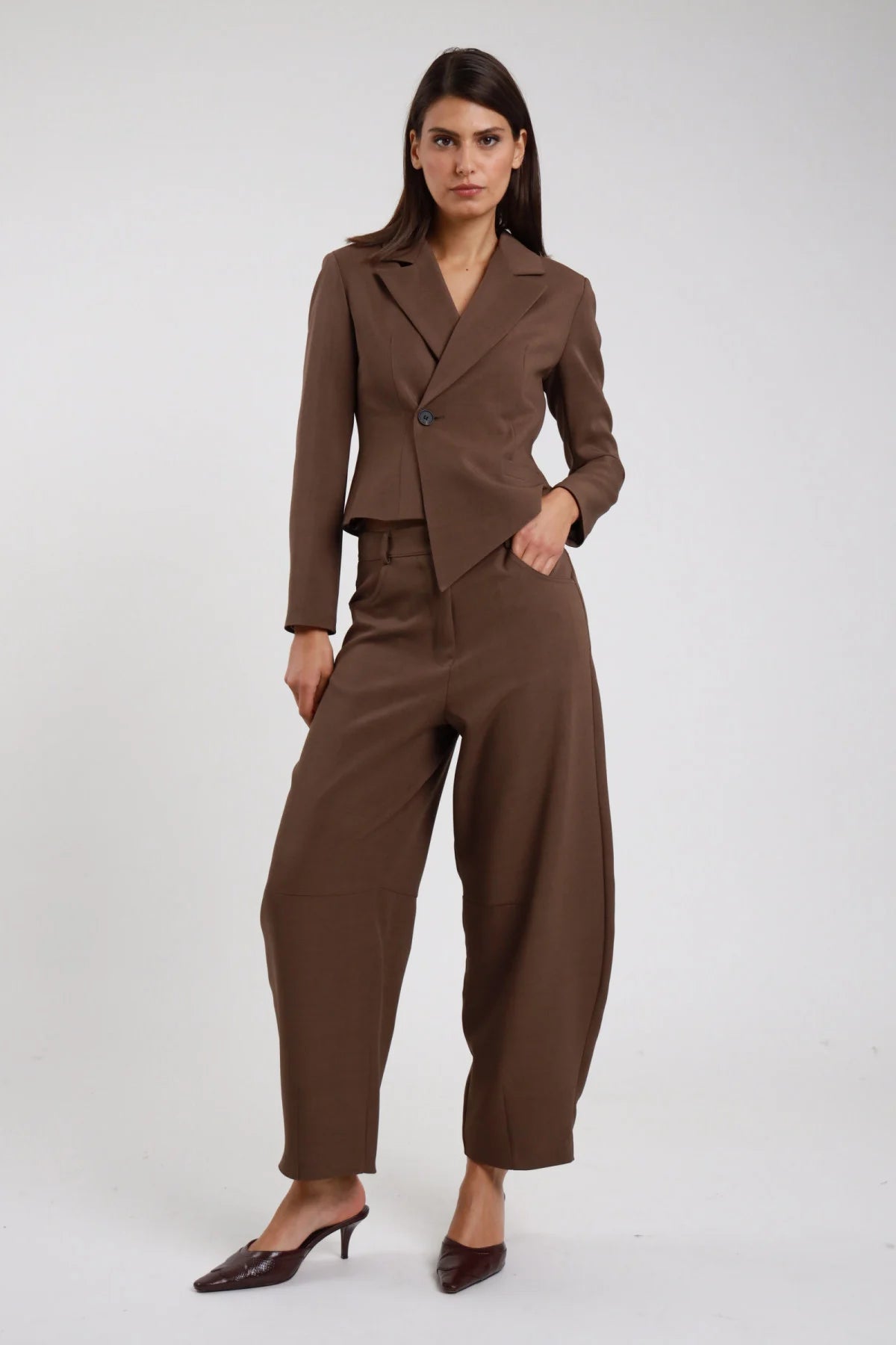 Pantalone Ovetto marrone cioccolato tabacco vita alta passanti cintura forma barrel scultorea pancia ampia orlo stretto caviglia frontale intera posa statica mano tasca sguardo frontale - modella frontale intera posa statica mano tasca sguardo frontale capelli castani sfondo bianco blazer asimmetrico marrone coordinato sabot marrone croco tacco kitten