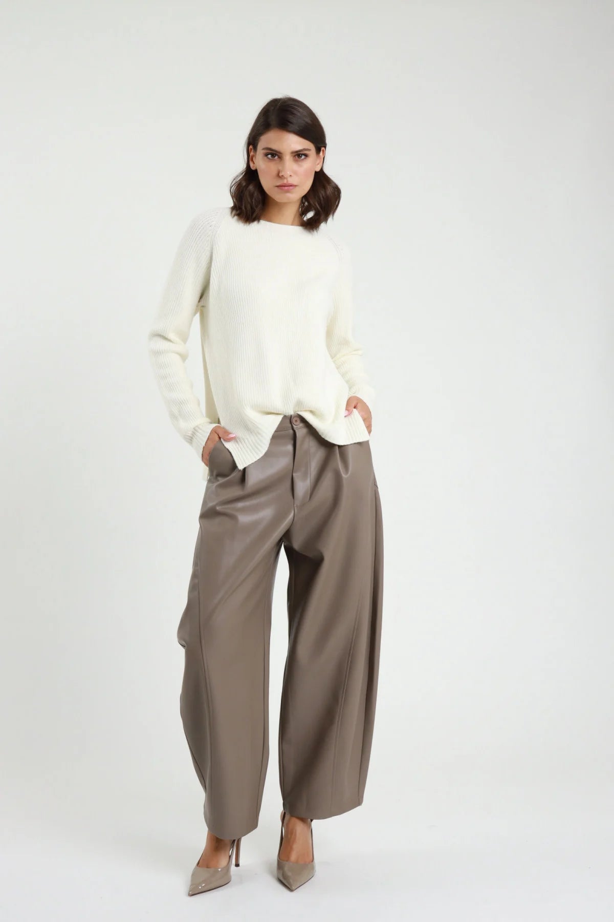 Pantalone Barrel Ecopelle tortora talpa vita alta pinces gamba barrel scultorea 7/8 cropped tasche oblique frontale intera in piedi - modella frontale intera mani tasche sguardo frontale capelli castani scuri sfondo bianco maglione oversize bianco panna décolleté nude tacco