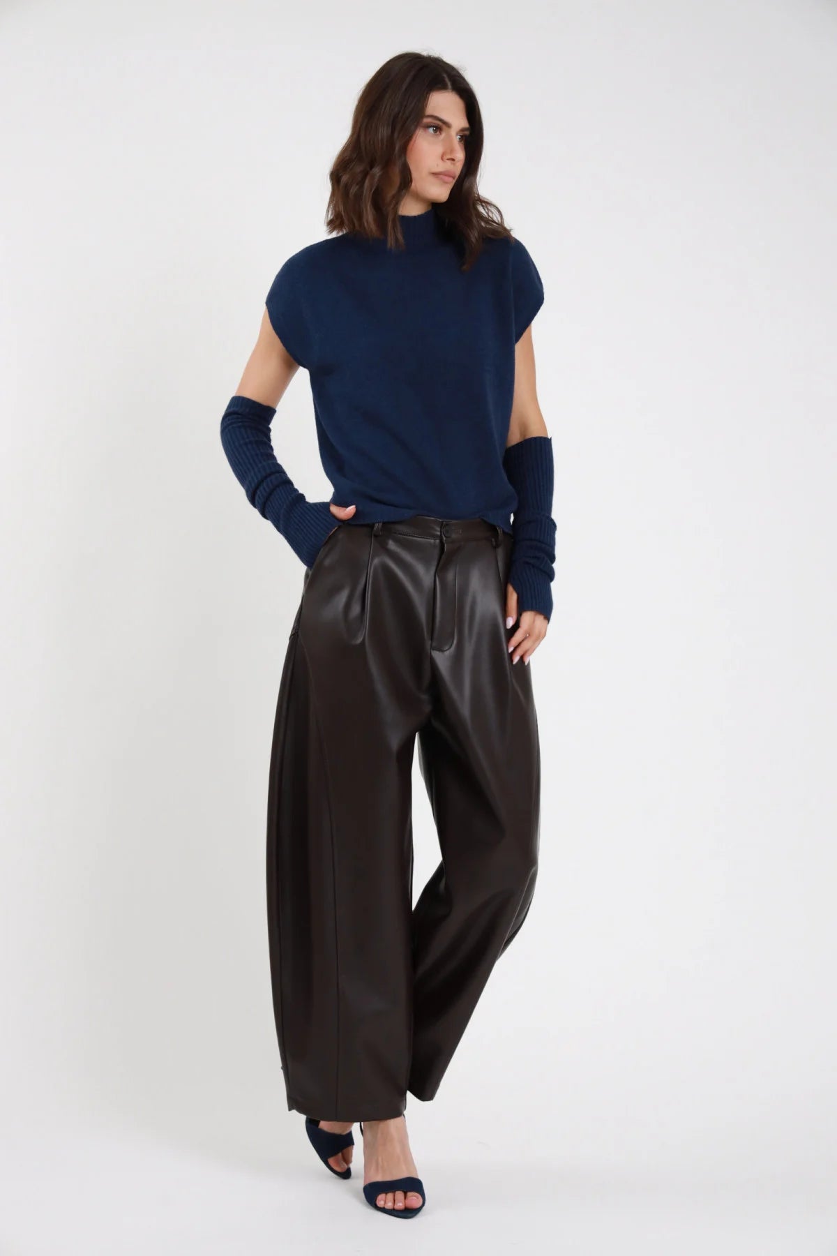 Pantalone Barrel Ecopelle marrone scuro cioccolato vita alta pinces gamba barrel scultorea 7/8 cropped tasche oblique frontale intera in piedi - modella frontale intera mano tasca sguardo alto laterale capelli castani scuri sfondo bianco top navy cut-out manica sandalo navy tacco