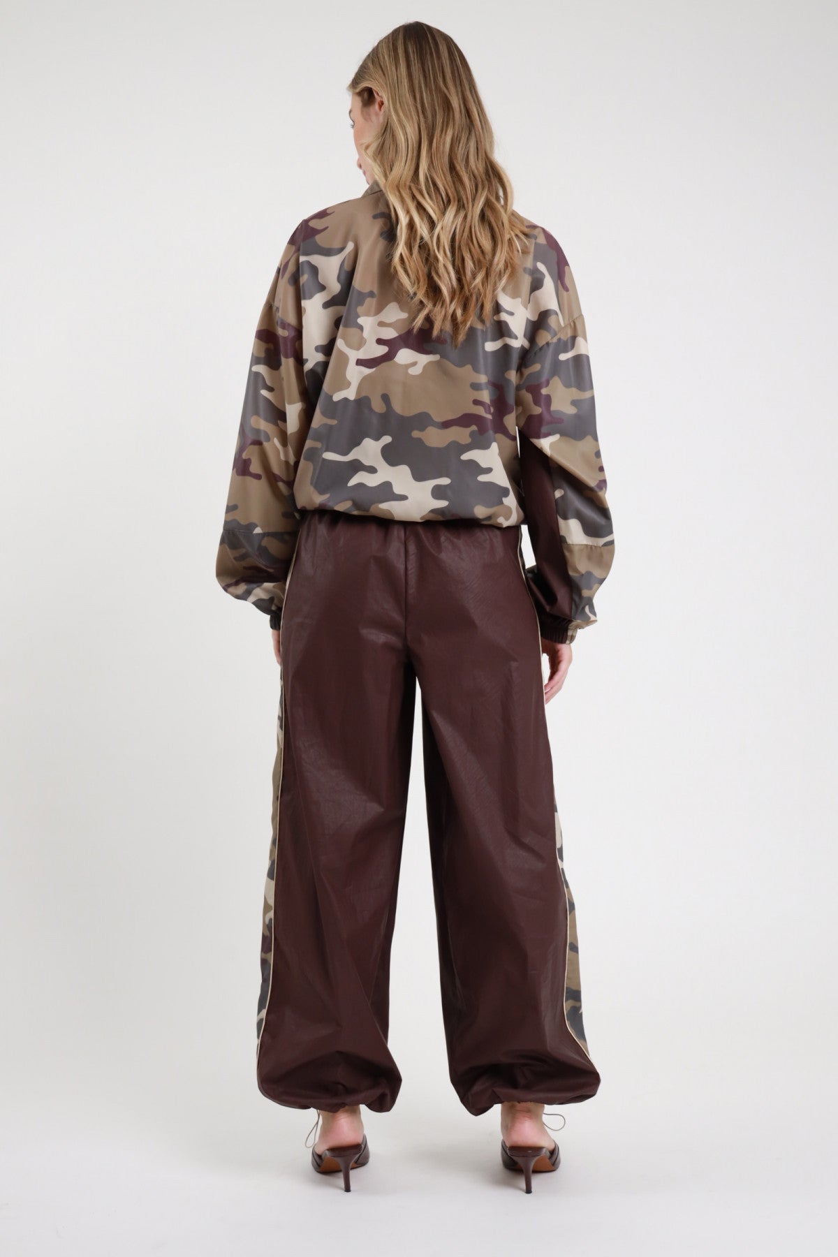 Pantalone Banda Camouflage cioccolato bordeaux 100% nylon banda camouflage laterale profilo beige gamba palazzo fondo balloon posteriore intera - modella intera posteriore capelli biondi ondulati sfondo bianco bomber over mimetico camouflage retro abbinato mule tacco kitten croco bordeaux