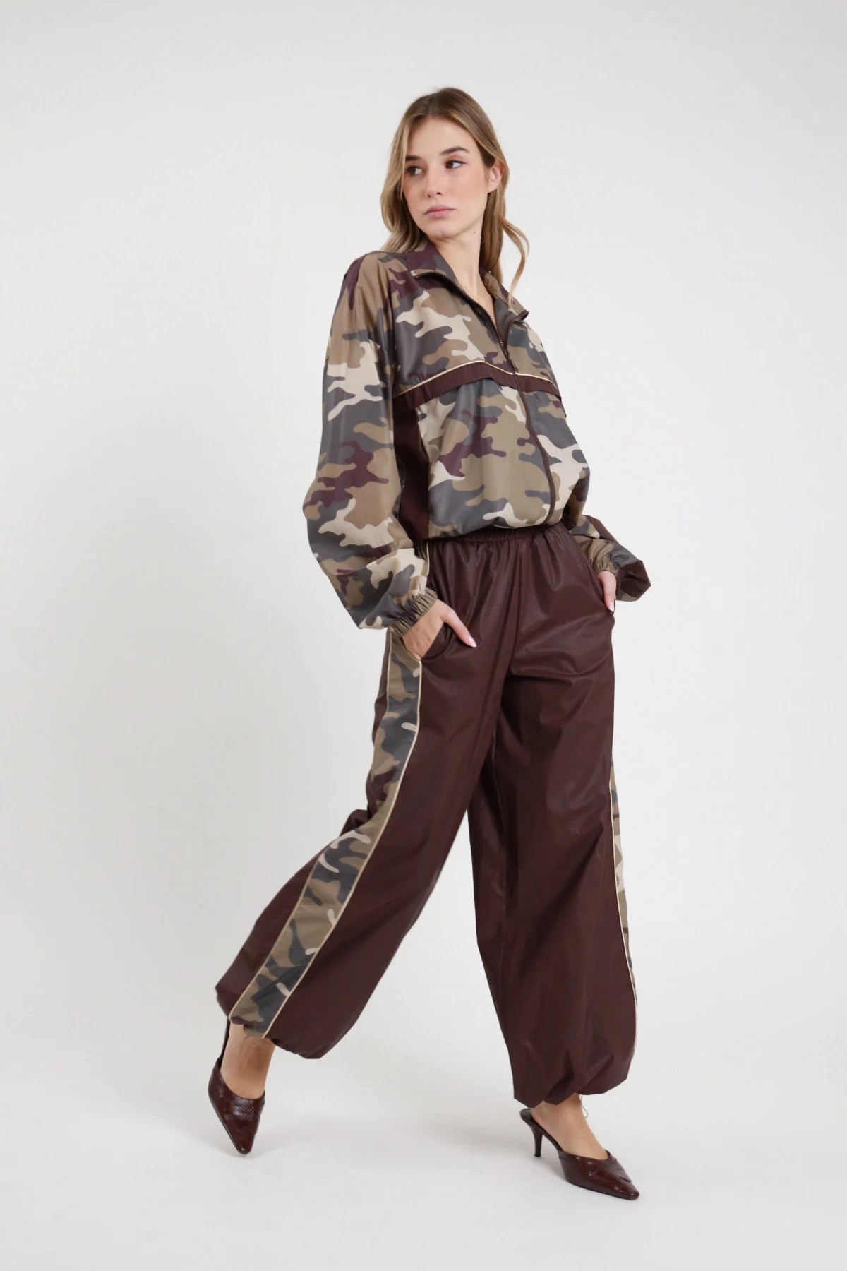 Pantalone Banda Camouflage cioccolato bordeaux 100% nylon banda camouflage marrone verde khaki profilo beige gamba palazzo balloon completo coordinato bomber mimetico frontale 3/4 posa in cammino - modella intera frontale 3/4 posa in cammino capelli biondi ondulati sguardo frontale sfondo bianco total look bomber over mimetico pantalone banda camouflage mule tacco kitten croco bordeaux