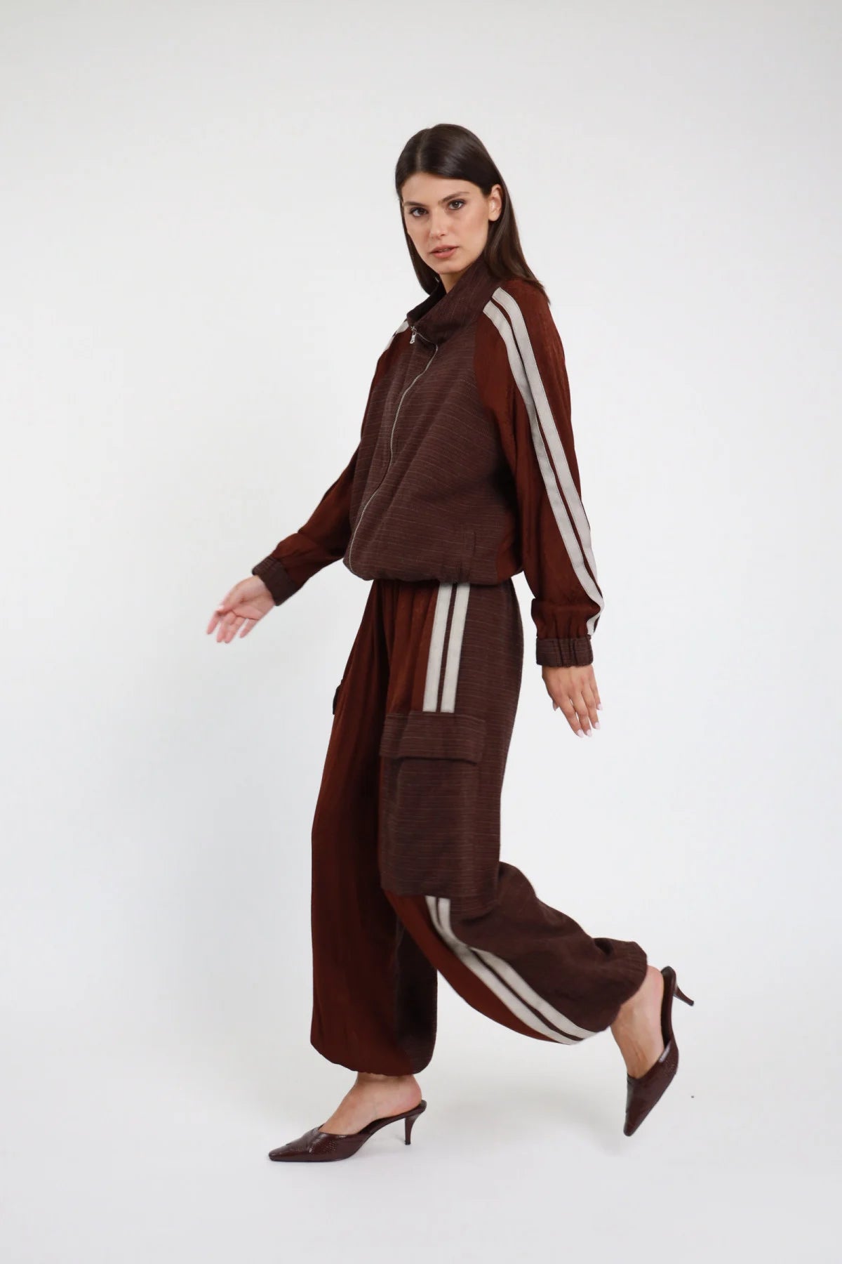 Pantalone Bande cioccolato bordeaux 55% rayon bande doppie beige panna laterali gamba palazzo fluida fondo balloon elastico caviglia laterale posa in cammino - modella intera laterale posa in cammino capelli castani lisci sfondo bianco total look bomber pantalone bande cioccolato mule tacco kitten croco bordeaux