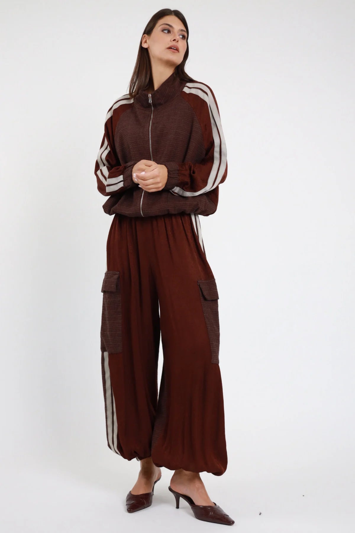 Pantalone Bande cioccolato bordeaux 55% rayon vita elastica alta tasche cargo bande doppie beige panna gamba palazzo balloon completo coordinato bomber bande frontale intera - modella intera frontale 3/4 mani intrecciate sguardo alto capelli castani lisci sfondo bianco total look bomber pantalone bande cioccolato mule tacco kitten croco bordeaux