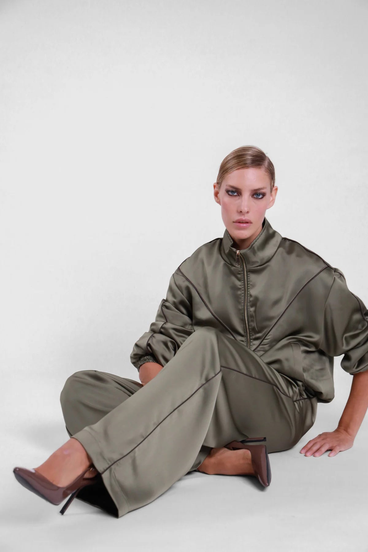 Pantalone piping Susy Mix verde oliva effetto satinato, modella seduta con dettaglio dei profili laterali scuri