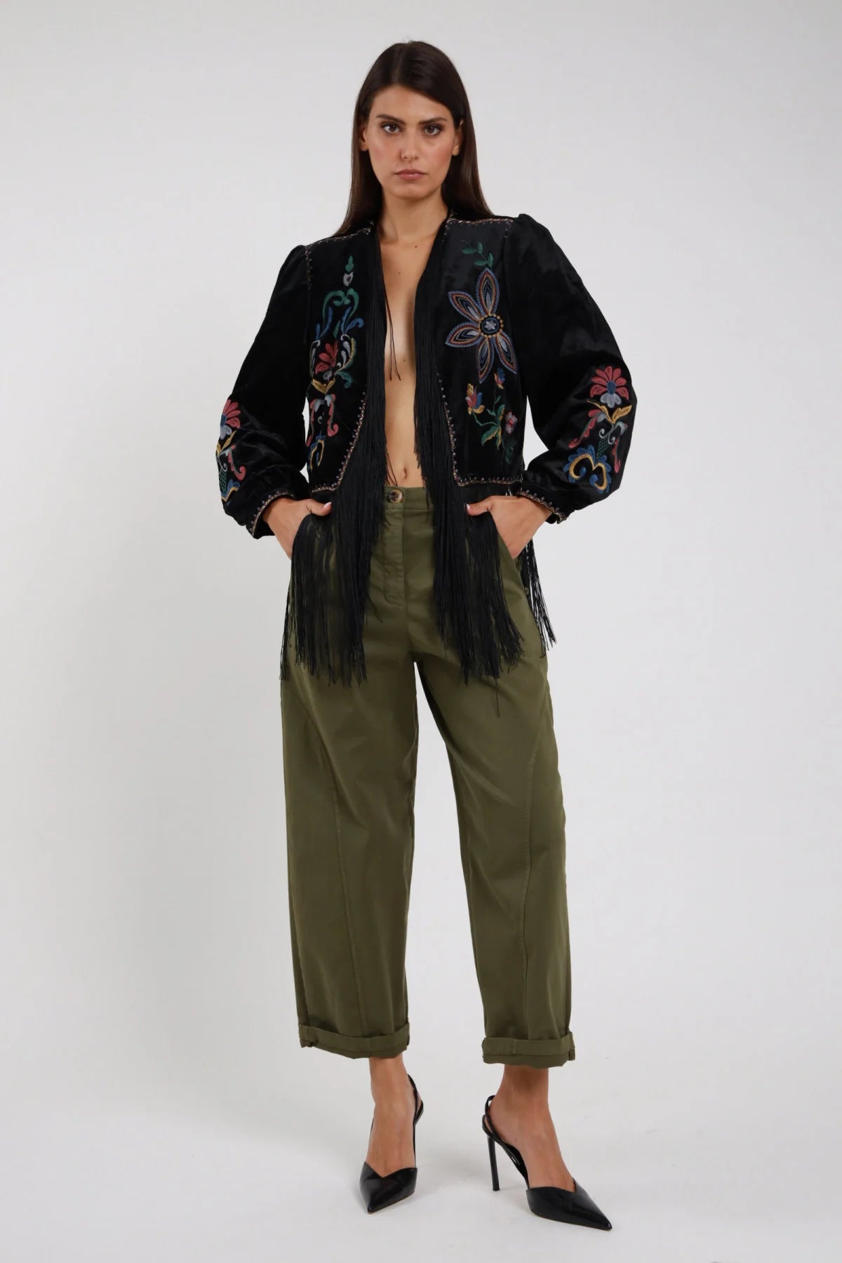 Pantaloni Tasconi Dietro verde militare kaki vita alta piega frontale gamba barrel carrot risvolto frontale intera posa statica mani tasche sguardo camera coordinata giacchino ricamato frange nero - modella frontale intera posa statica mani tasche sguardo camera capelli castani sfondo bianco giacchino ricamato frange nero décolleté neri tacco alto