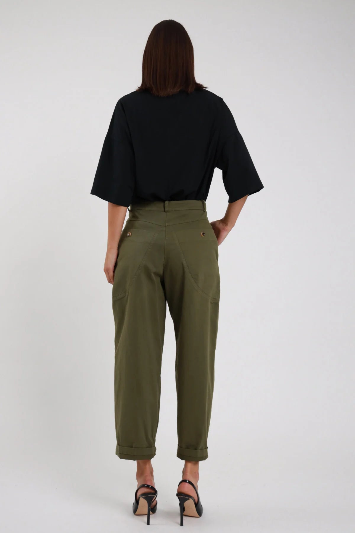 Pantaloni Tasconi Dietro verde militare kaki retro 2 tasconi posteriori grandi bottoni dorati cintura posteriore strutturata gamba barrel risvolto retro intera schiena - modella retro intera capelli castani sfondo bianco t-shirt nera oversize crop décolleté neri slingback tacco alto