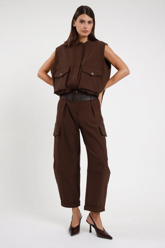 Pantalone Cargo Tasconi Vita Alta marrone cioccolato 78% viscosa vita alta passanti cintura larga pieghe davanti strutturate 2 tasconi laterali cargo bottone risvolto fondo gamba barrel ballon cropped caviglia frontale intera - modella intera frontale posa mani fianchi sguardo frontale intenso capelli castani lisci sfondo bianco gilet marrone coordinato cintura ecopelle nera slingback vernice nera