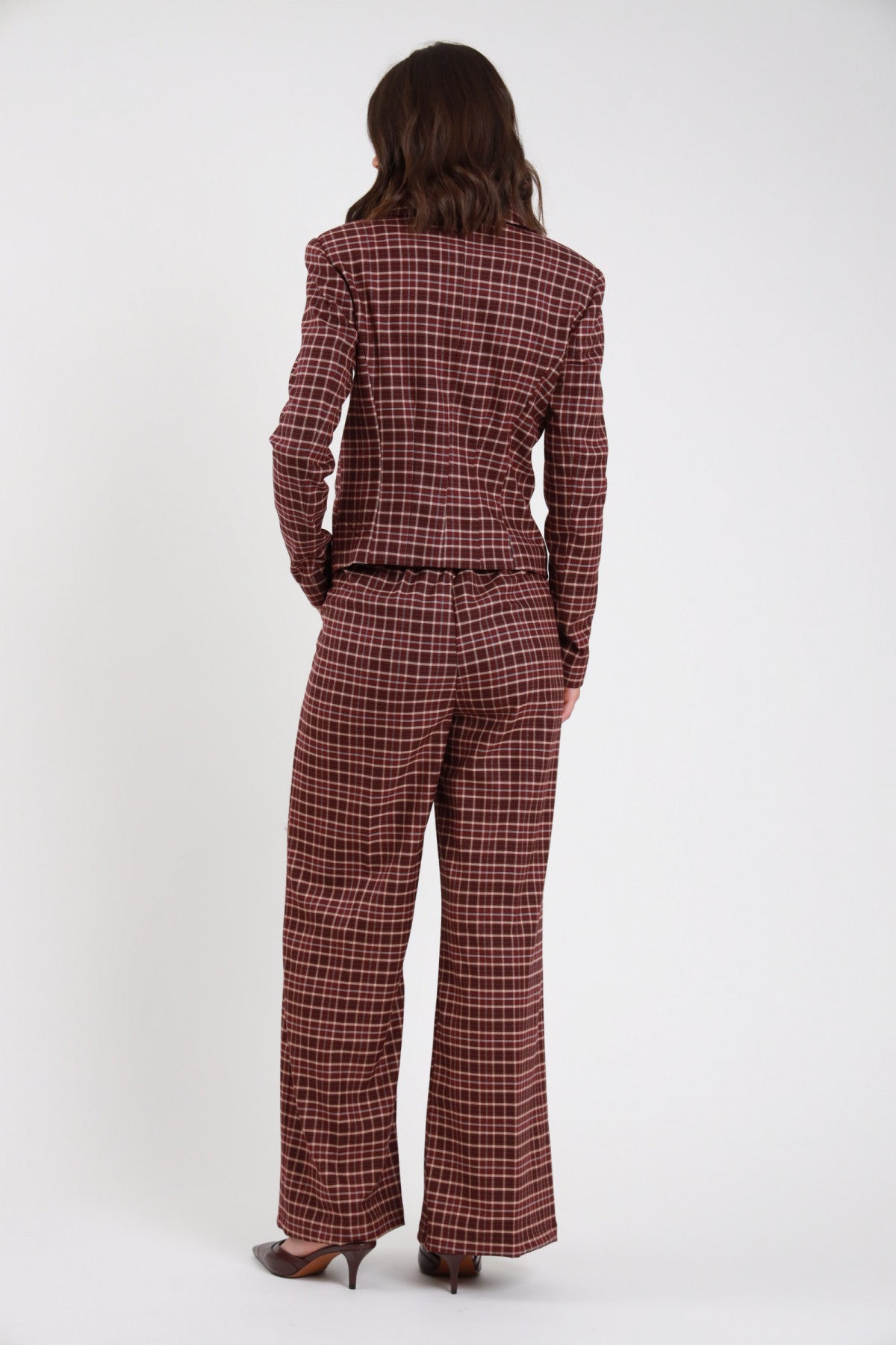 Pantalone Check tartan quadri bordeaux ruggine wide leg palazzo maxi vita elastico retro intera con Blazer Check bordeaux - modella retro intera mani schiena fianchi sguardo laterale capelli castani scuri sfondo bianco blazer check bordeaux kitten heel bordeaux vernice