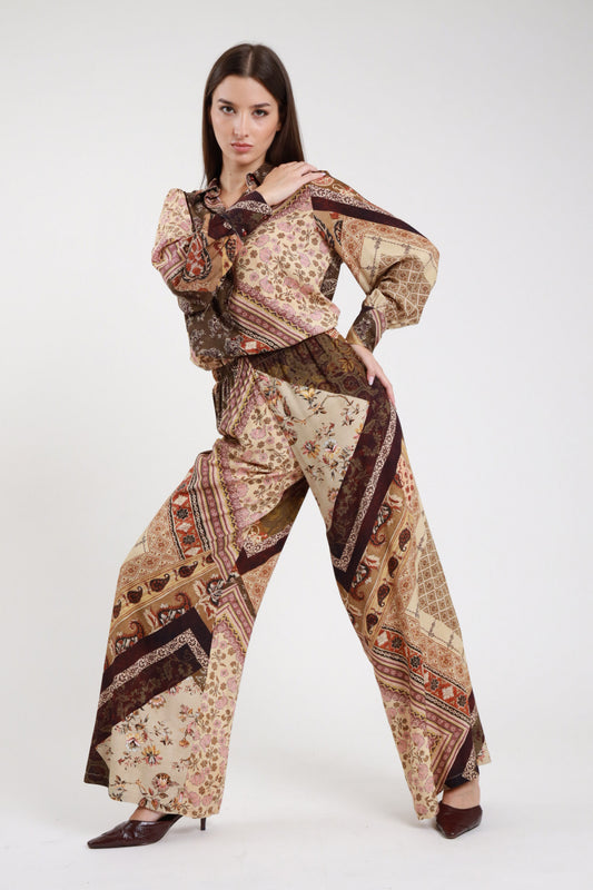 Pantalone fantasia patchwork paisley baroque floral prugna bordeaux vinaccia panna ecru frontale intera con camicia fantasia coordinata vita alta elastico coulisse gamba wide leg palazzo ultrampia svasata maxi floor-length orlo dritto stivali marroni tacco - modella frontale intera sguardo frontale intenso con camicia fantasia coordinata stivali marroni tacco capelli castani lisci sfondo bianco