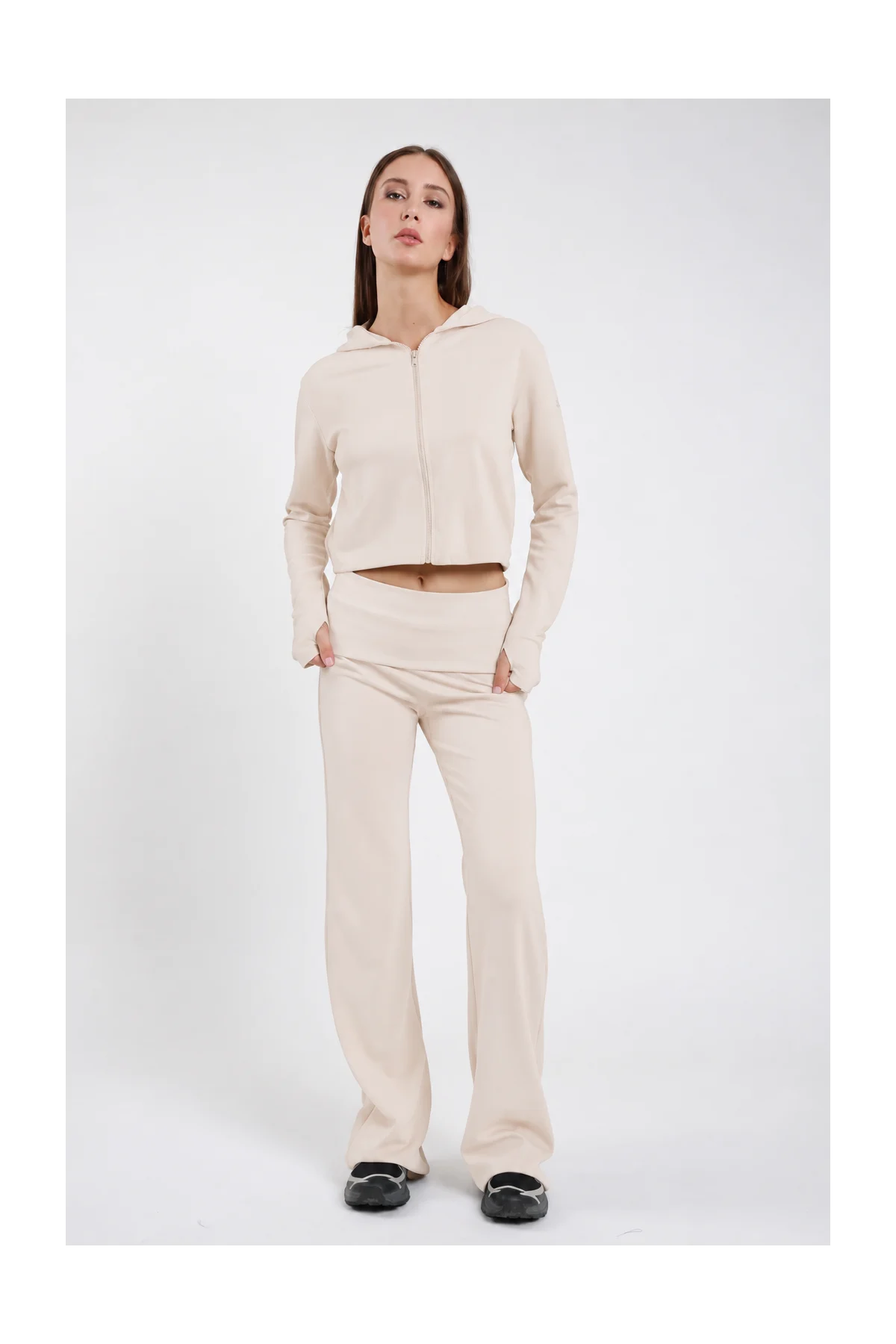 Pantaloni Flare DAYTHRU panna avorio elastico fold-over vita bassa logo SMX bianco coscia gamba flare bootcut silhouette scultorea frontale intera posa statica mani tasche sguardo frontale - modella frontale intera posa statica mani tasche sguardo frontale capelli castani lisci sfondo bianco felpa crop zip panna coordinata sabot neri