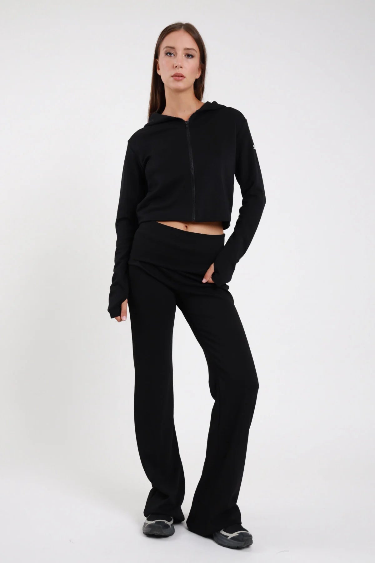 Pantaloni Flare DAYTHRU nero elastico fold-over vita bassa logo SMX coscia gamba flare extra-ampio bootcut frontale intera posa statica mano tasca sguardo frontale - modella frontale intera posa statica mano tasca sguardo frontale capelli castani lisci sfondo bianco felpa crop zip nera coordinata foro pollice visibile sneakers nere chunky