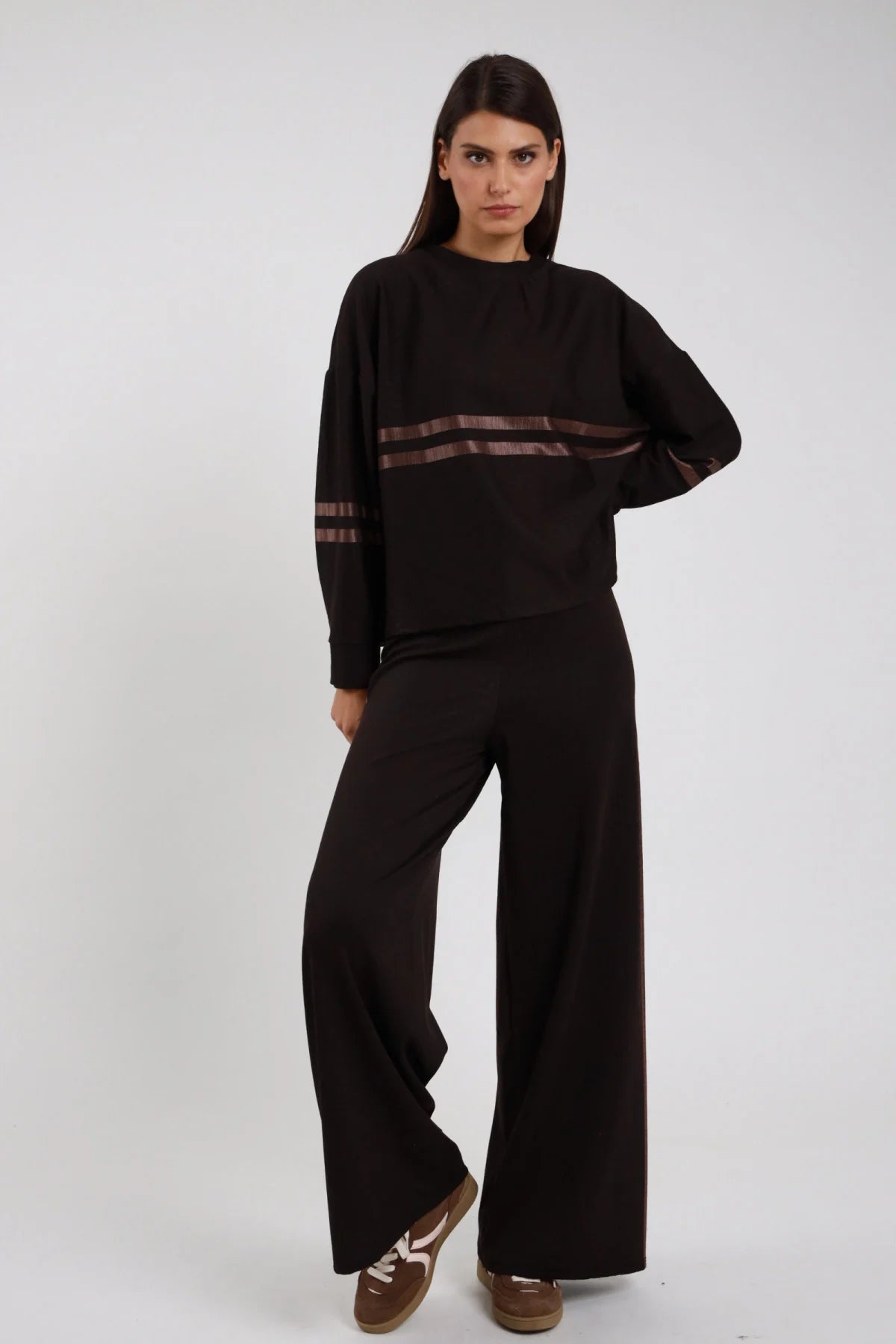 Pantaloni Animalier Bande Satinate nero tinta unita 2 bande satinate marrone bronzo laterali wide leg palazzo vita elastico - modella intera frontale posa mani fianchi sguardo frontale intenso capelli castani lisci sfondo bianco felpa nera coordinata sneakers marroni