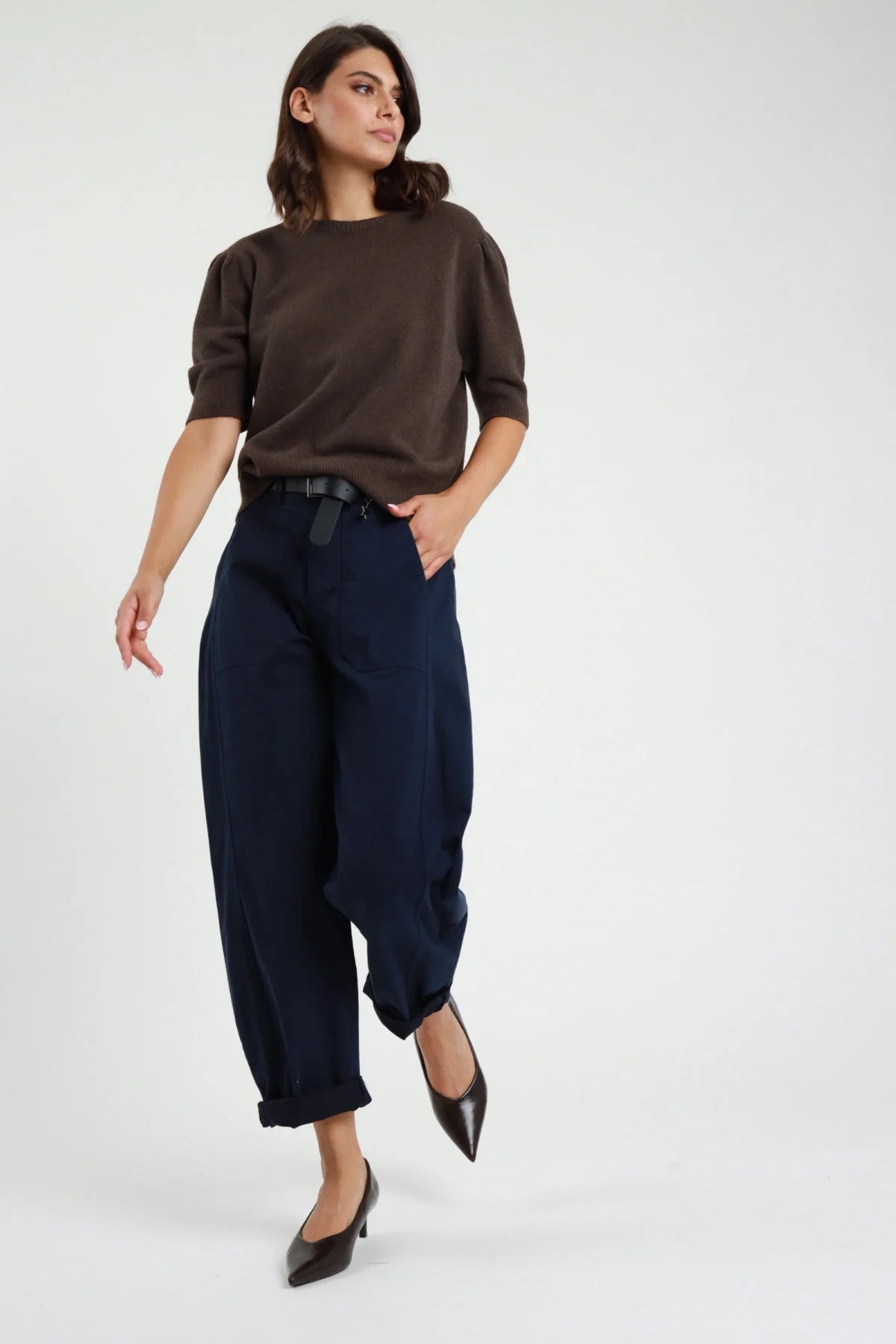 Pantalone Stellina ovetto balloon vita alta pinces risvolto affusolato avorio panna frontale intera - modella frontale intera sguardo frontale capelli castani scuri sfondo bianco cardigan nero bottoni argento cintura nera loafer neri