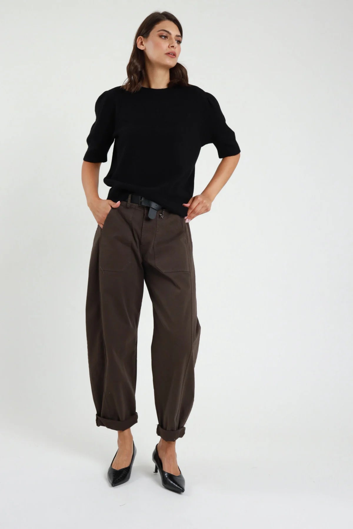 Pantalone Stellina ovetto balloon vita alta pinces risvolto affusolato antracite grigio scuro frontale intera - modella frontale intera sguardo laterale capelli castani scuri sfondo bianco maglia manica corta lilla cintura nera décolleté neri kitten heel