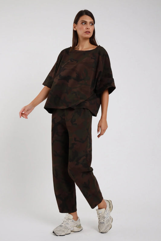 Pantalone Ovetto Mimetico camouflage marrone cioccolato nero sfumato 95% cotone vita alta elastico gamba balloon ovetto tasche laterali - modella intera 3/4 laterale posa dinamica gamba avanzata sguardo laterale capelli castani lisci sfondo bianco blusa oversize mimetica coordinata sneakers chunky beige bianche