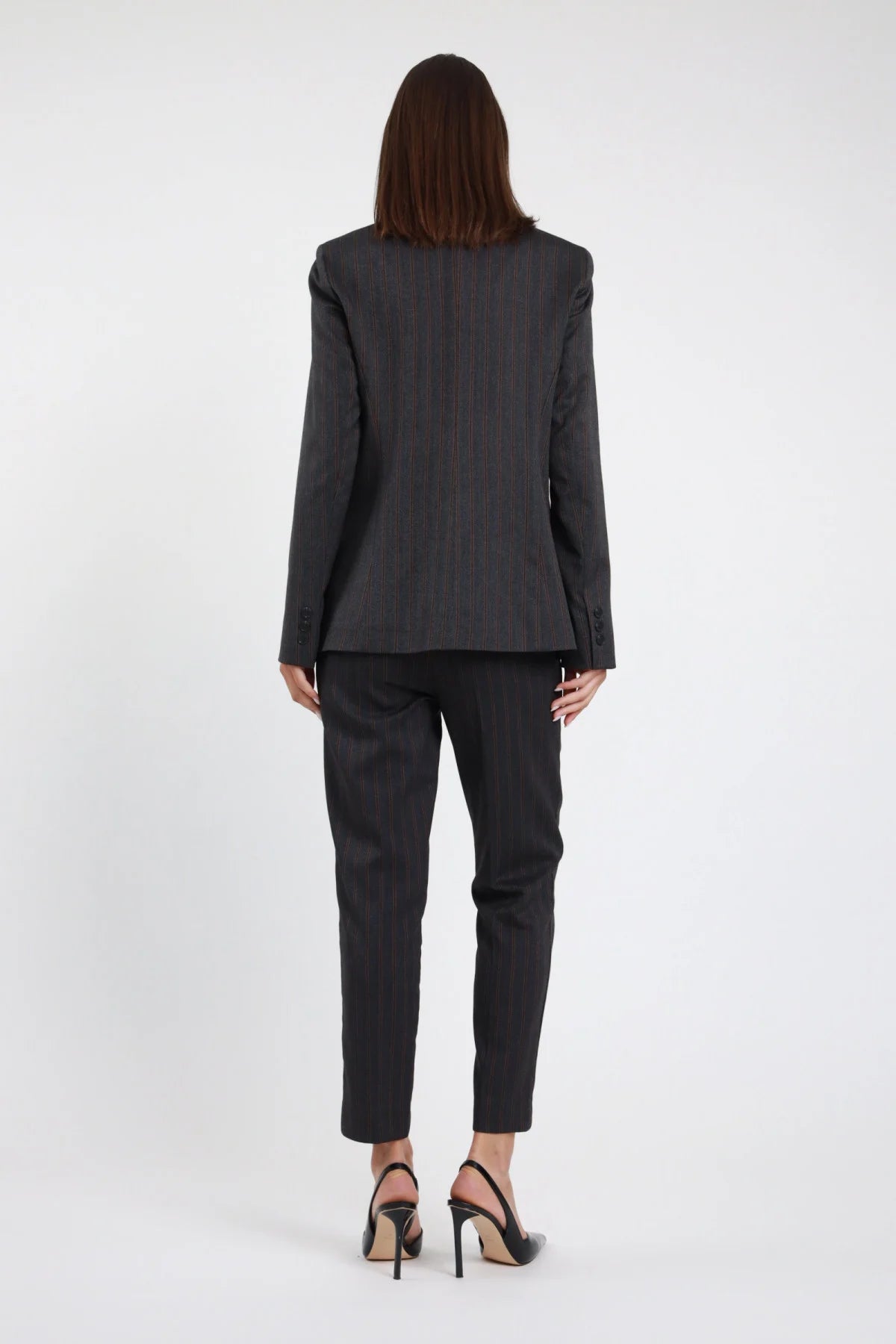 Pantalone slim gessato Susy Mix Pre-Fall grigio antracite pinstripe bordeaux gamba slim affusolata caviglia cuciture sartoriali retro posteriore intera - modella posteriore intera capelli scuri lisci sfondo bianco blazer doppiopetto gessato coordinato tailleur slingback neri abbinati