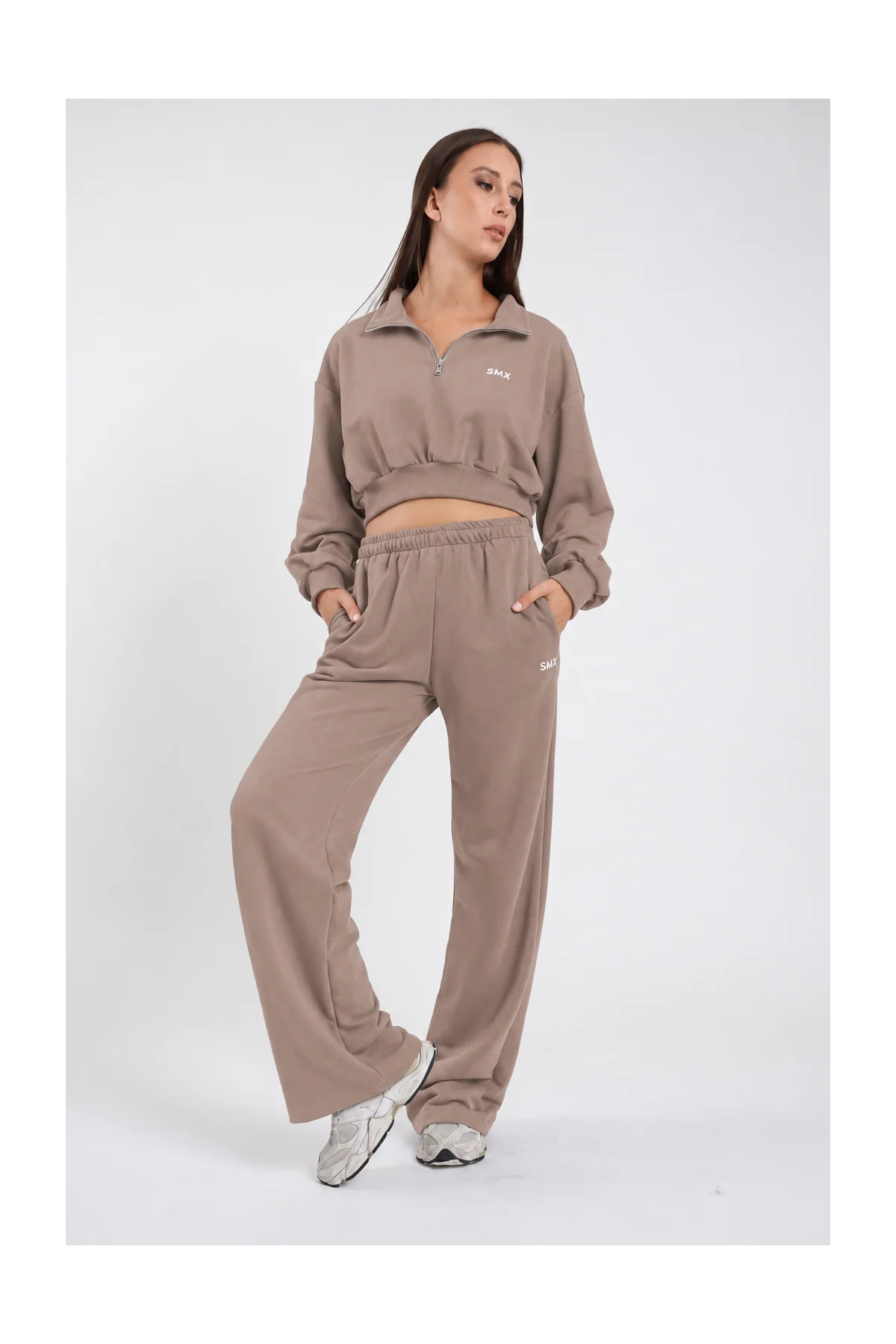 Pantalone Wide Leg DAYTHRU grigio taupe tortora elastico vita logo SMX bianco coscia gamba wide jogger tasche laterali frontale intera posa statica mano fianco sguardo laterale - modella frontale intera posa statica mano fianco sguardo laterale capelli castani lisci sfondo bianco felpa crop 1/2 zip taupe coordinata sneakers bianche