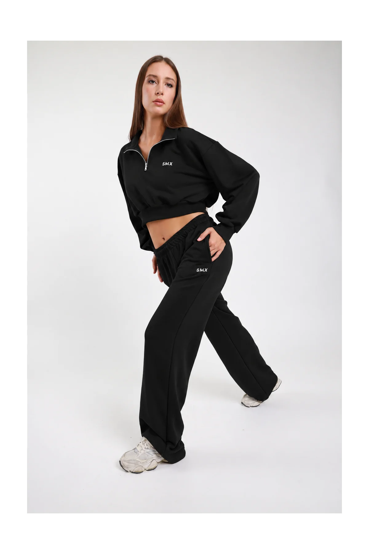 Pantalone Wide Leg DAYTHRU nero elastico vita logo SMX bianco coscia a contrasto gamba wide jogger tasche laterali frontale intera posa dinamica gamba alzata mano tasca sguardo basso - modella frontale intera posa dinamica gamba alzata mano tasca sguardo basso capelli castani lisci sfondo bianco felpa crop 1/2 zip nera coordinata sneakers bianche chunky