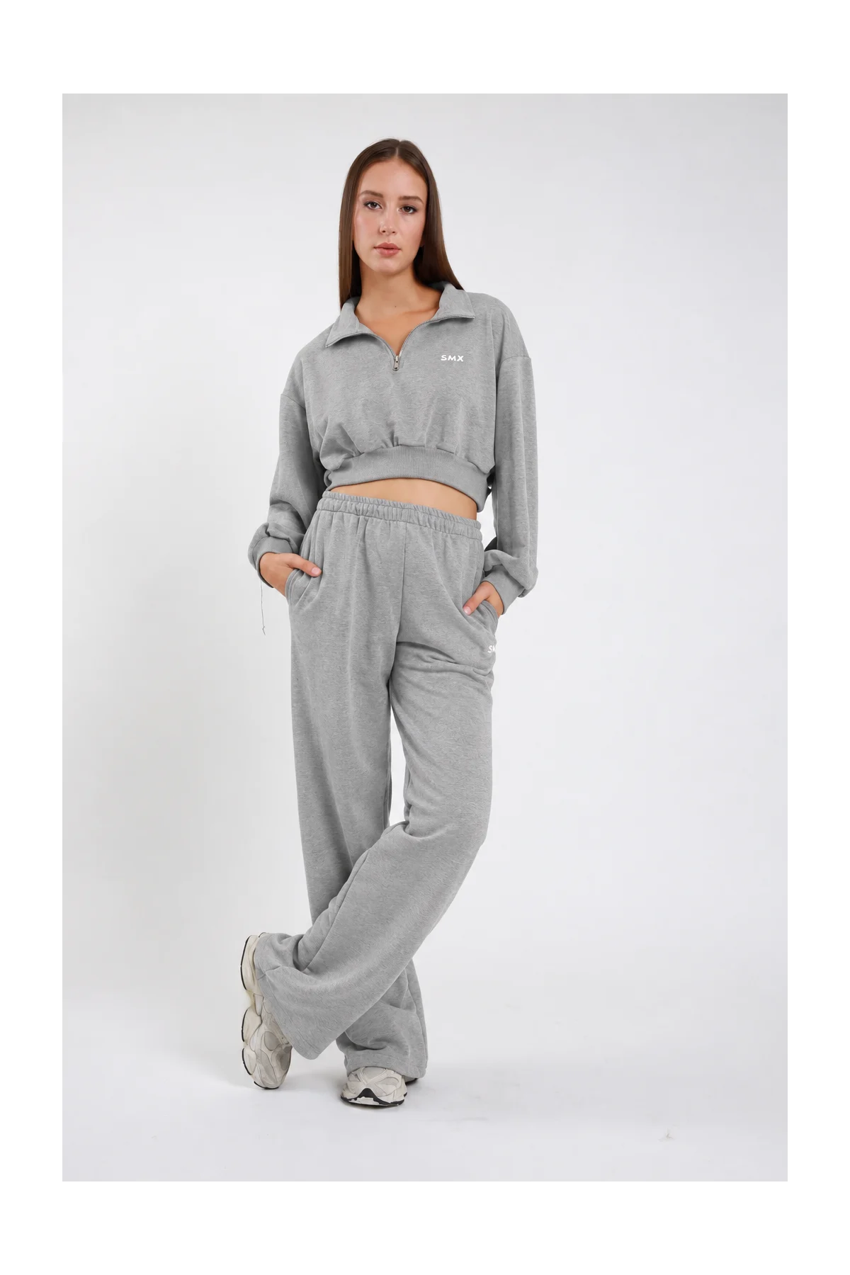 Pantalone Wide Leg DAYTHRU grigio melange chiaro elastico vita logo SMX bianco coscia gamba wide jogger tasche laterali frontale intera posa statica mani tasche sguardo frontale - modella frontale intera posa statica mani tasche sguardo frontale capelli castani lisci sfondo bianco felpa crop 1/2 zip grigio melange coordinata sneakers chunky grigio bianche